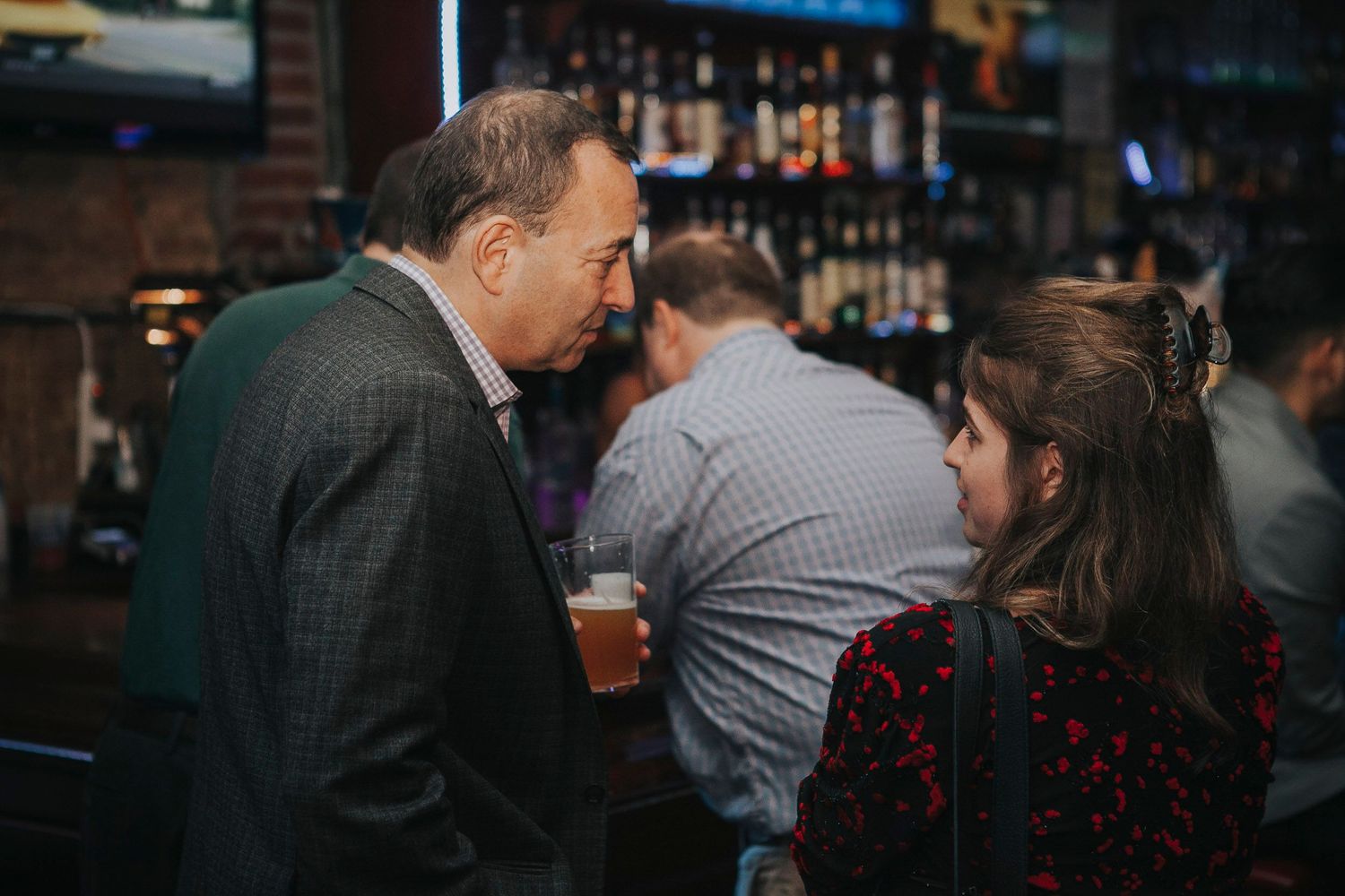 Man in suit holds a beer while conversing with a woman at a bar event.