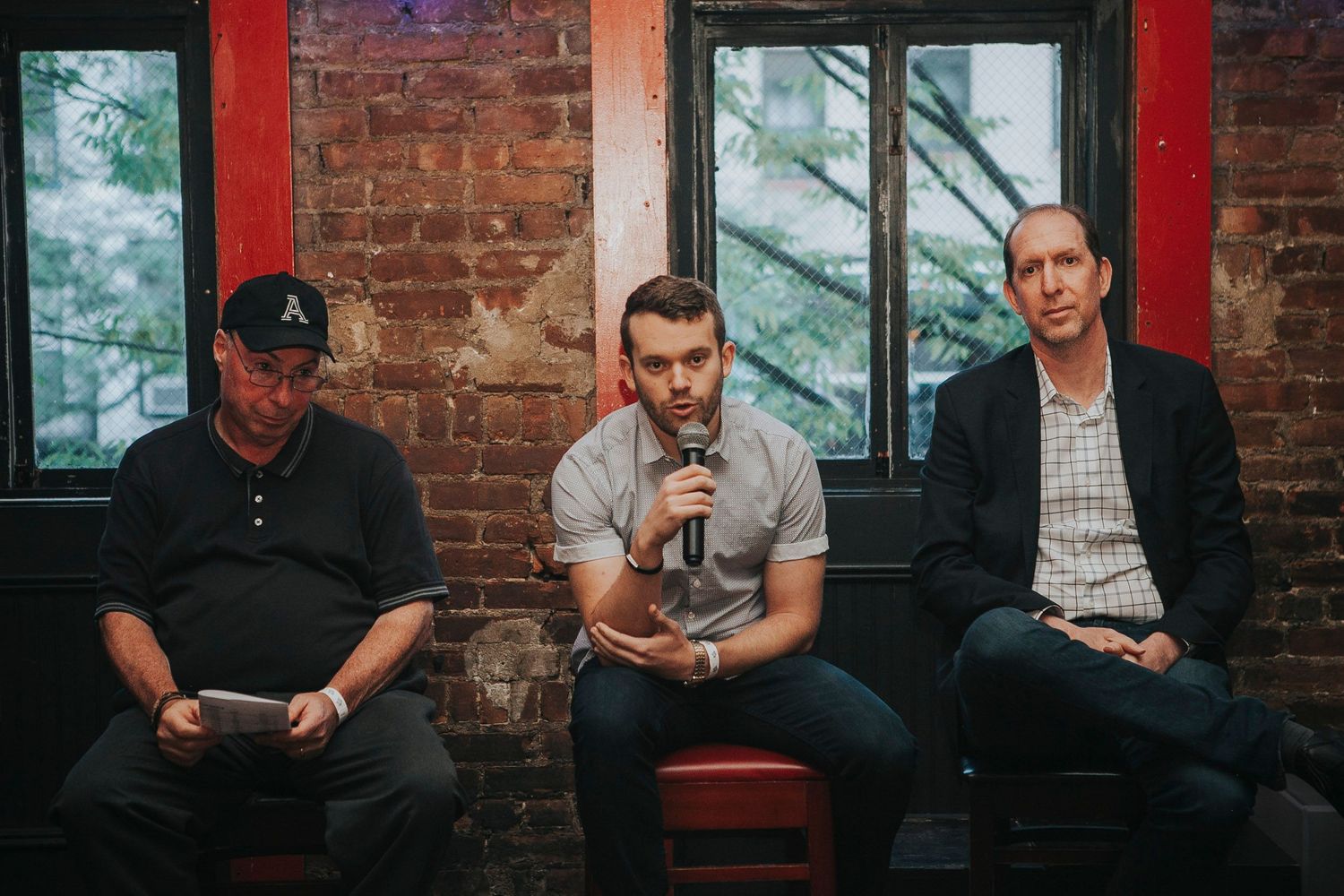 Three men sit together, one speaking into microphone at panel event.