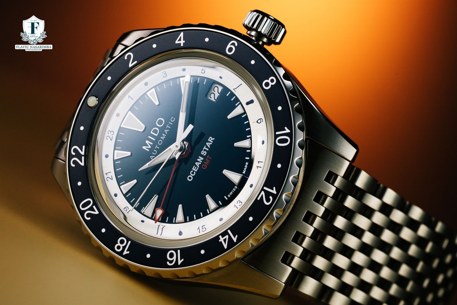 Mido Ocean Star GMT watch with navy blue dial on stainless steel bracelet against warm orange background.