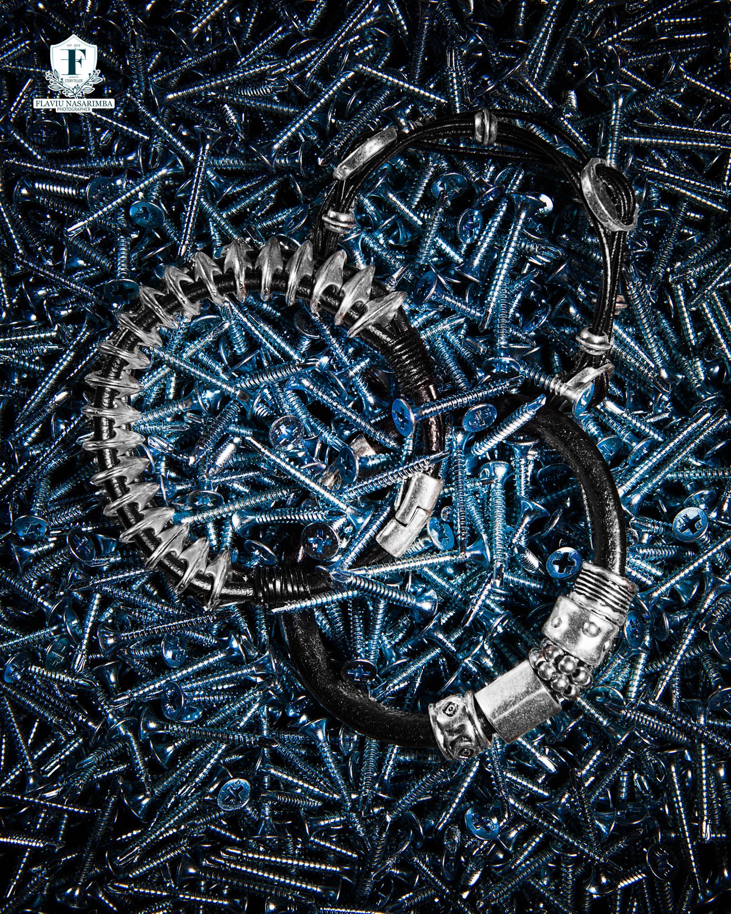 Black leather bracelet with silver spiral detail displayed on blue screws background.