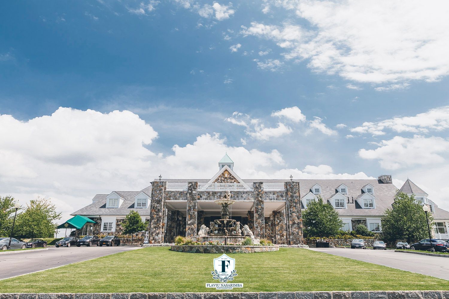 Elegant stone wedding venue exterior with fountain and manicured lawn under blue sky.