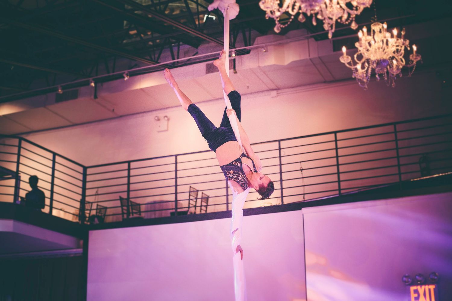 An aerial acrobat performs an inverted pose on silk fabric beneath a chandelier at an event.