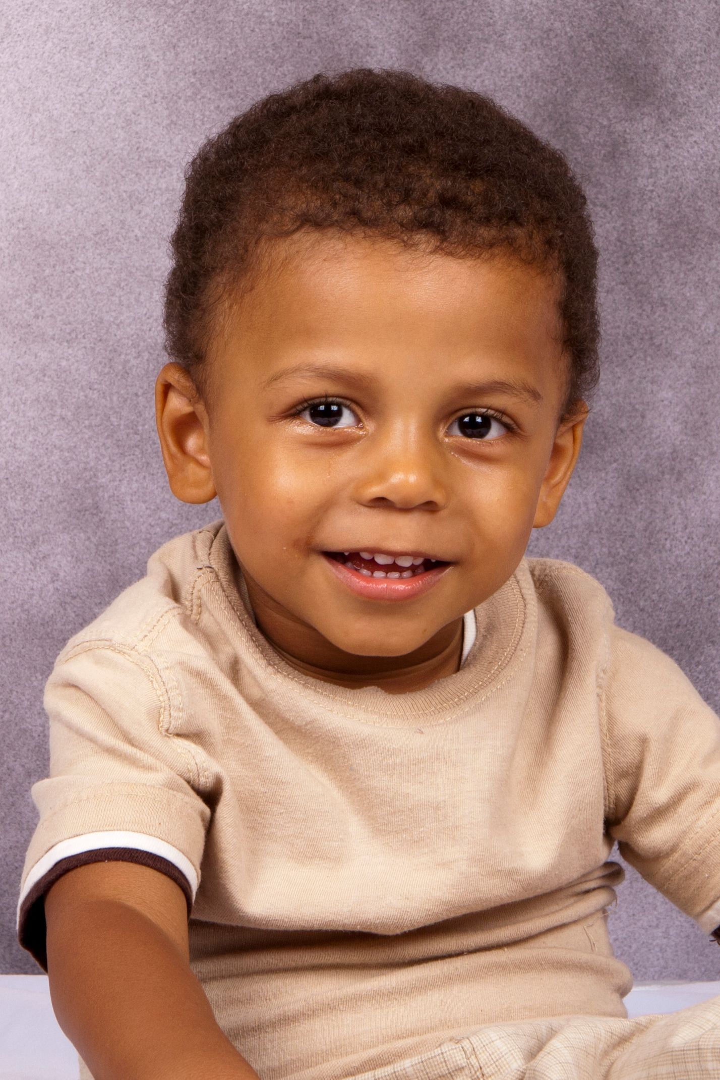 Adorable smiling toddler boy in beige shirt posing for studio portrait photo.