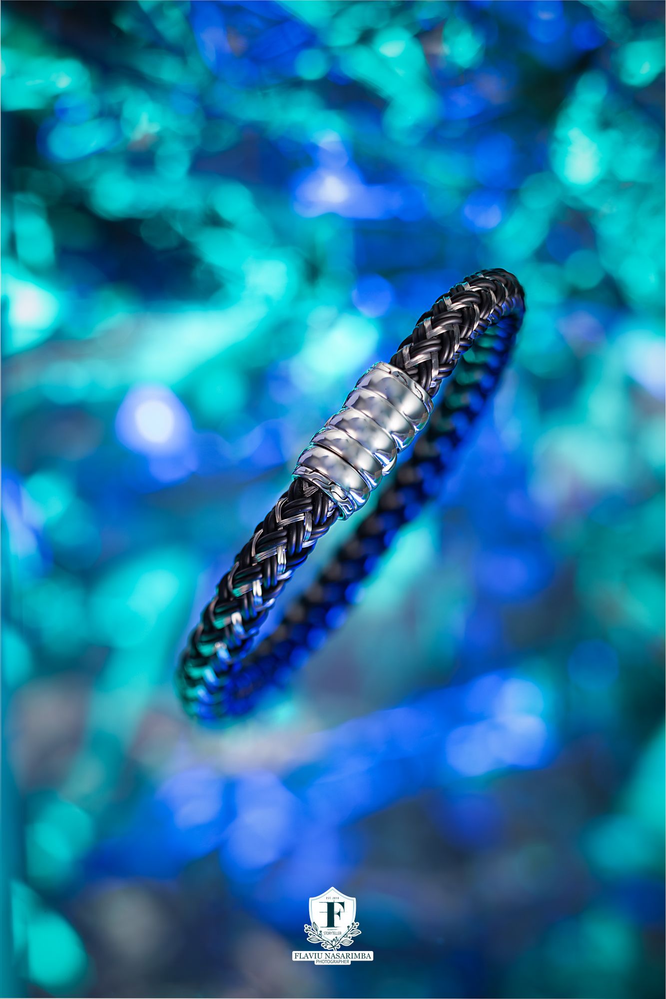 Dark braided leather bracelet with silver magnetic clasp on blue bokeh background.
