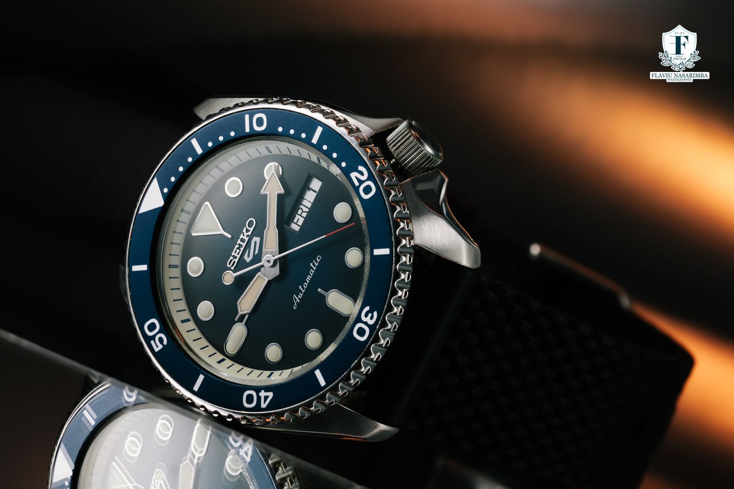 Seiko 5 Sports automatic diver watch with blue dial and bezel on black rubber strap in dramatic lighting.