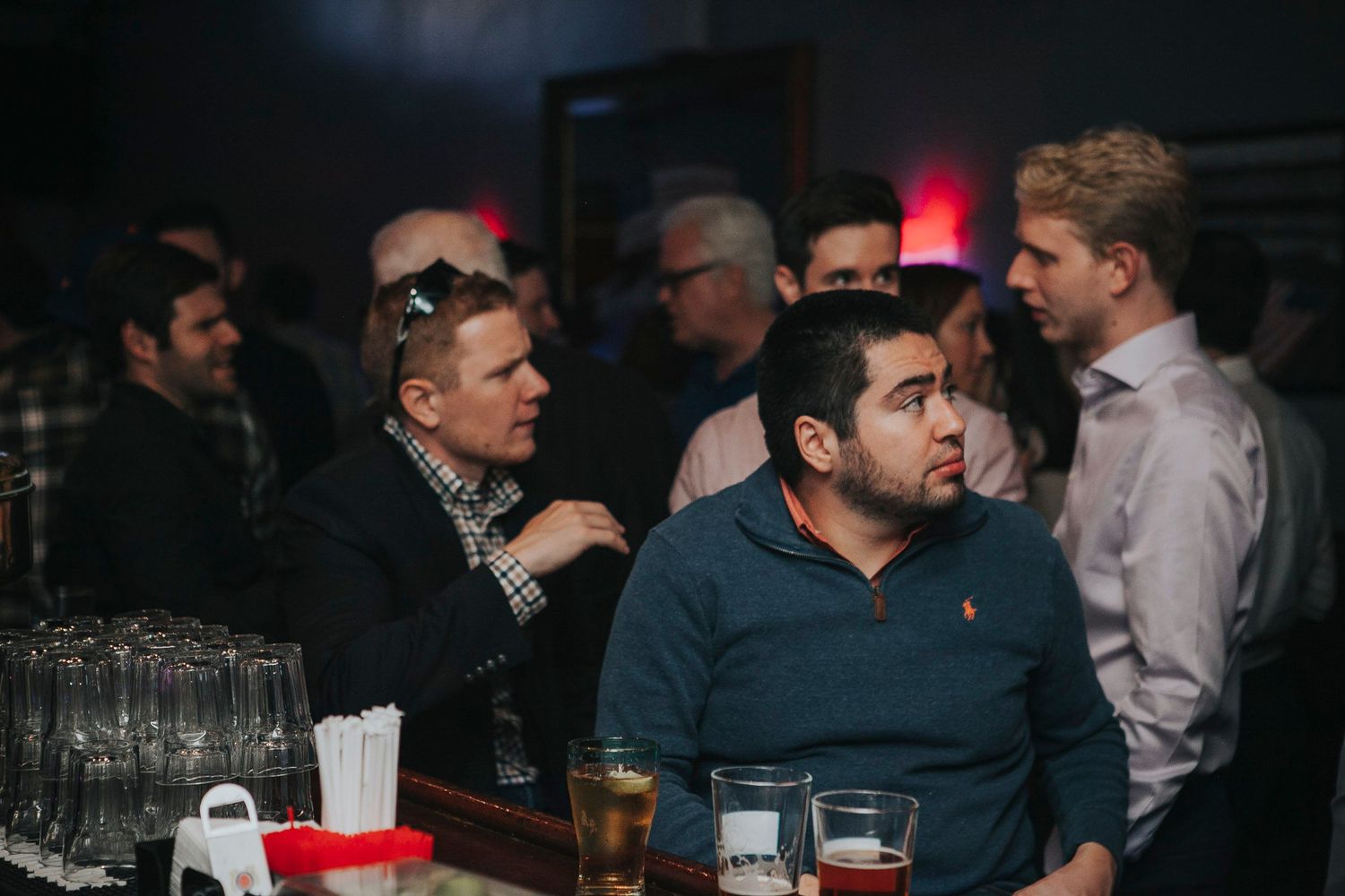 Men gather around a bar counter watching screens at a social event.