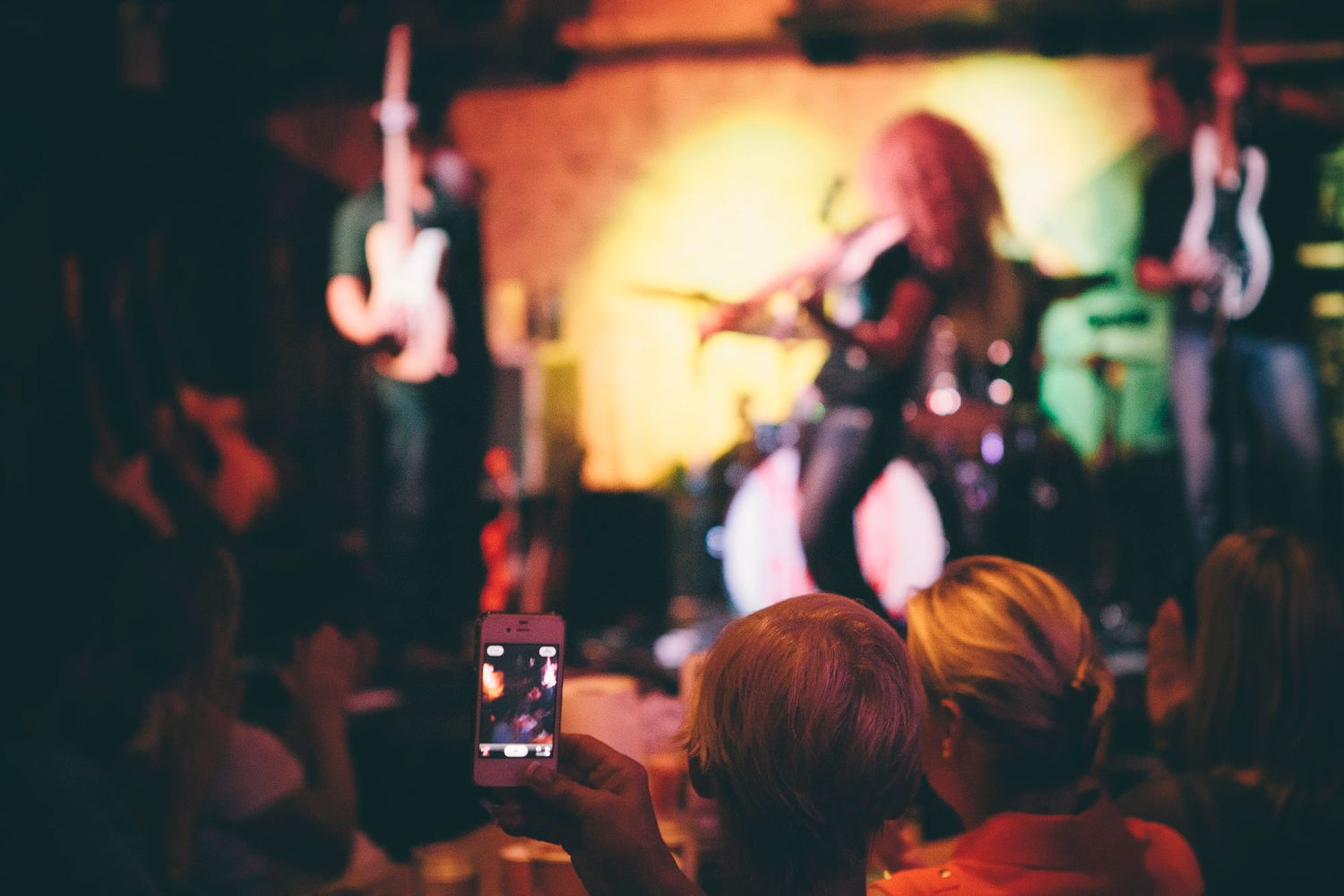 Audience member records live concert performance on smartphone in dimly lit music venue.