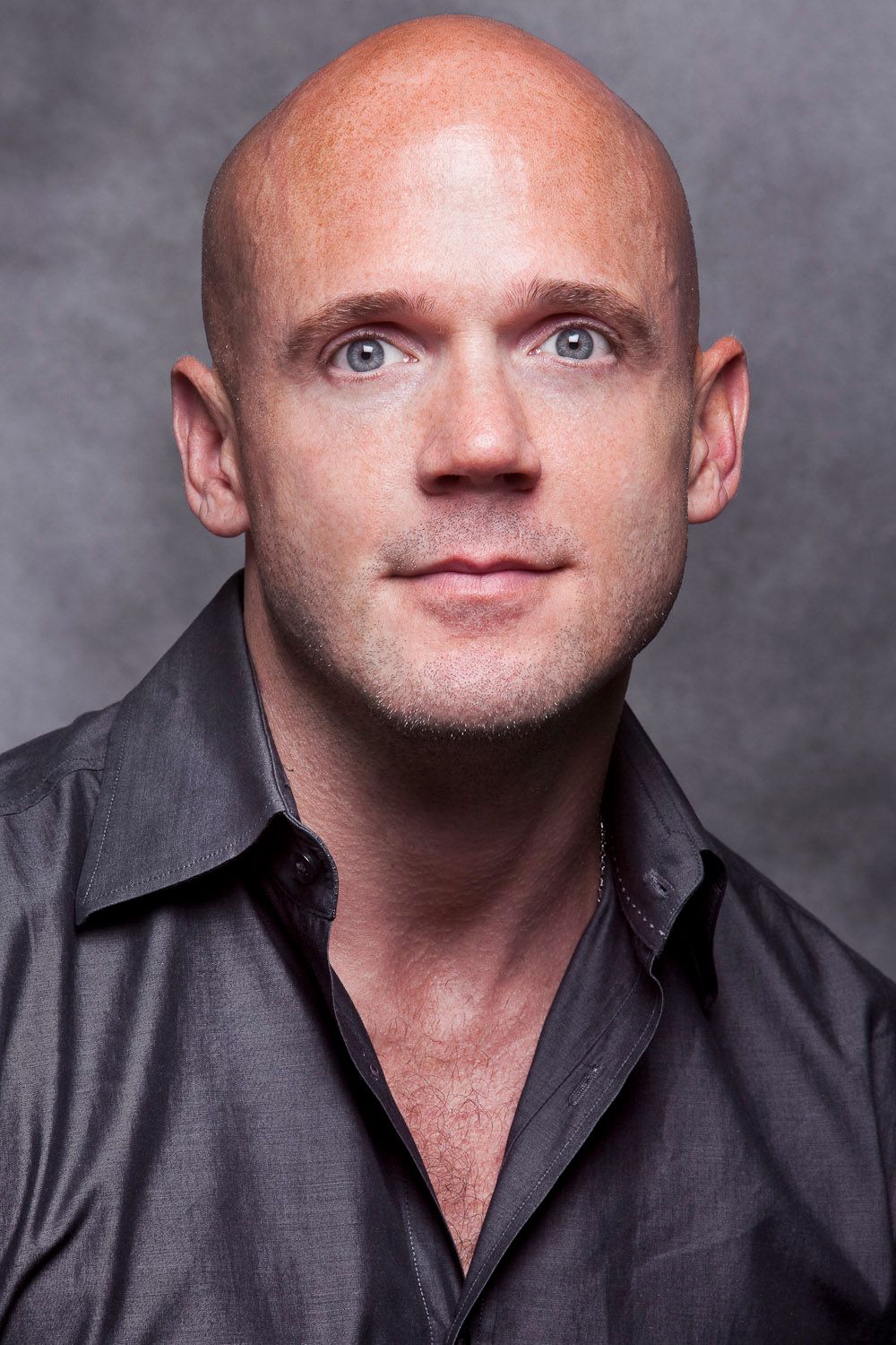 Bald man with blue eyes wearing a dark shirt posing for a professional headshot portrait.