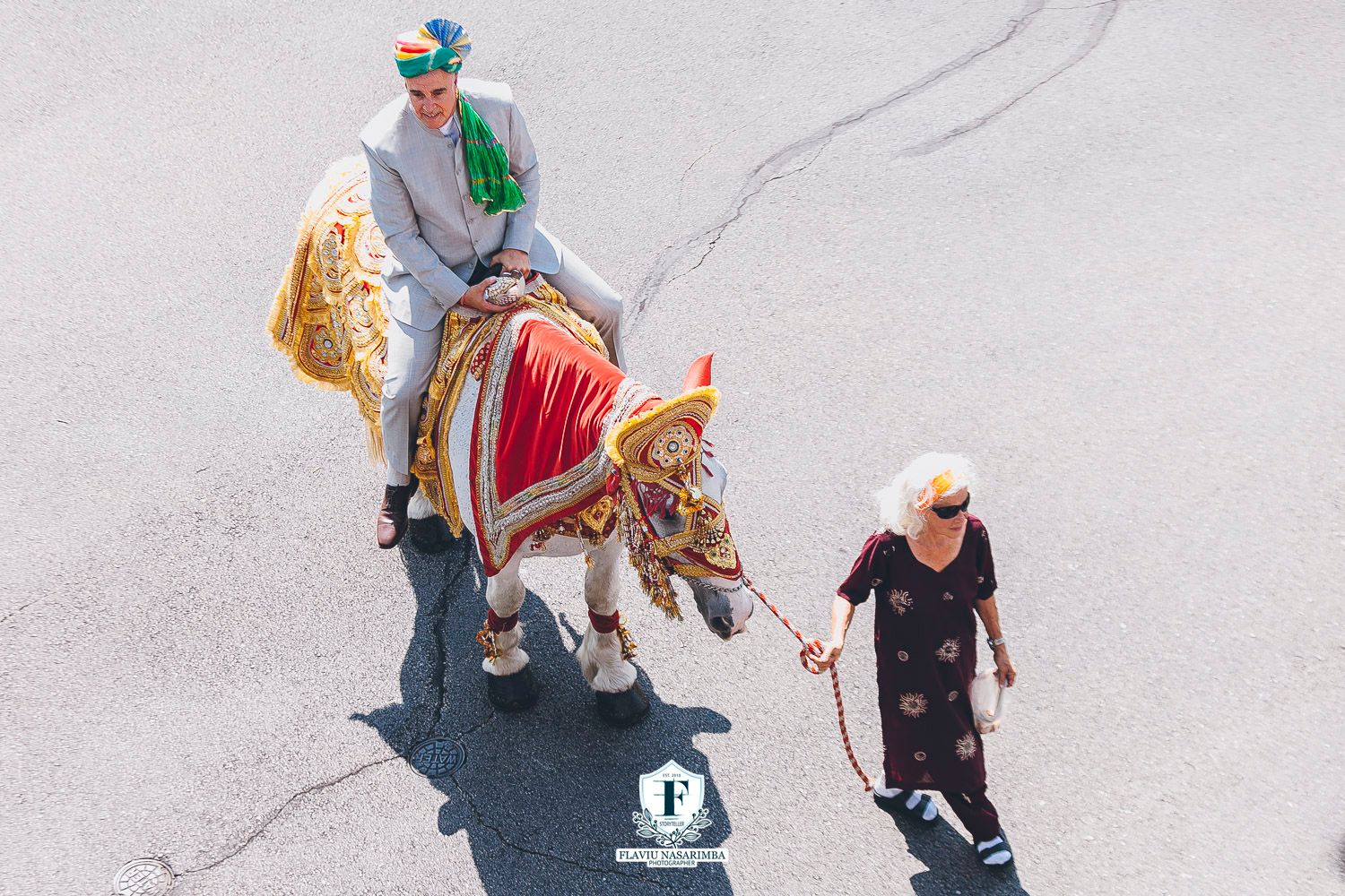 Aerial view of groom riding ornately decorated horse led by elderly woman at Indian wedding procession.