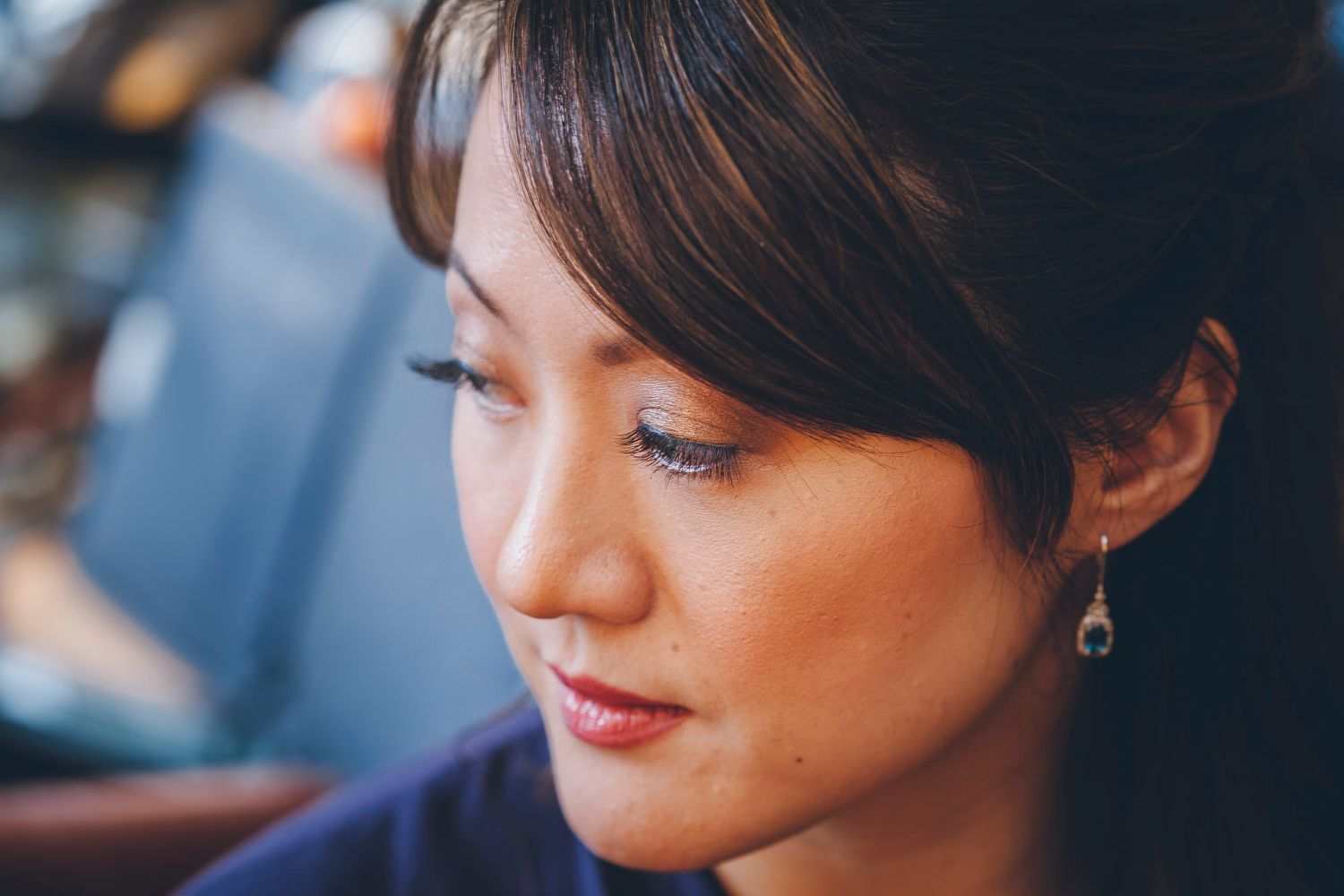 Close-up portrait of Asian woman with elegant drop earrings and subtle makeup looking downward thoughtfully.