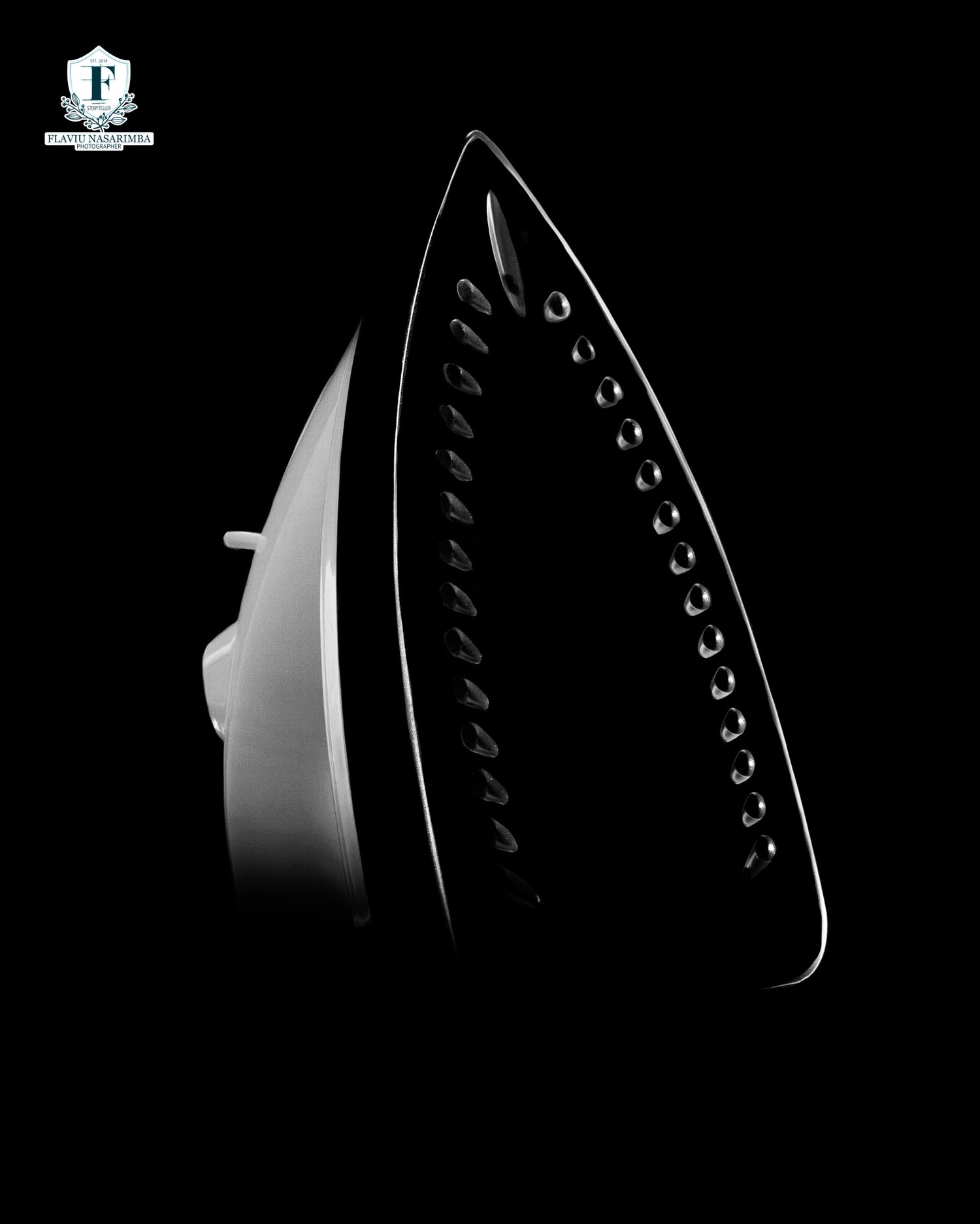 Side profile of a black and silver steam iron with steam holes on dark background.