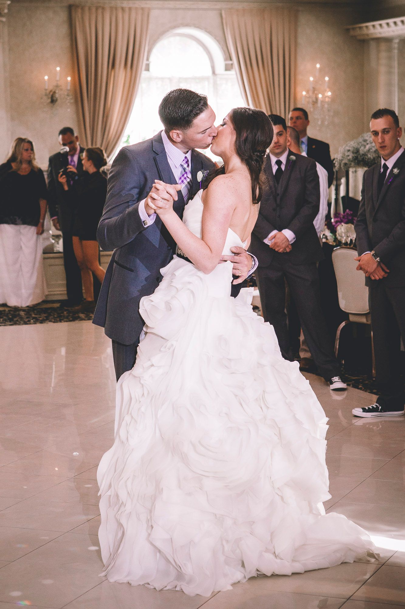 Bride and groom share a romantic kiss during their first dance at an elegant wedding reception.