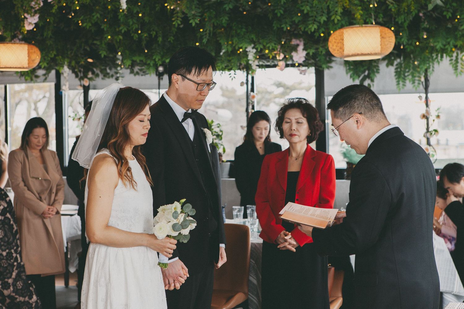 Bride and groom exchange vows before officiant with family guests watching the ceremony.