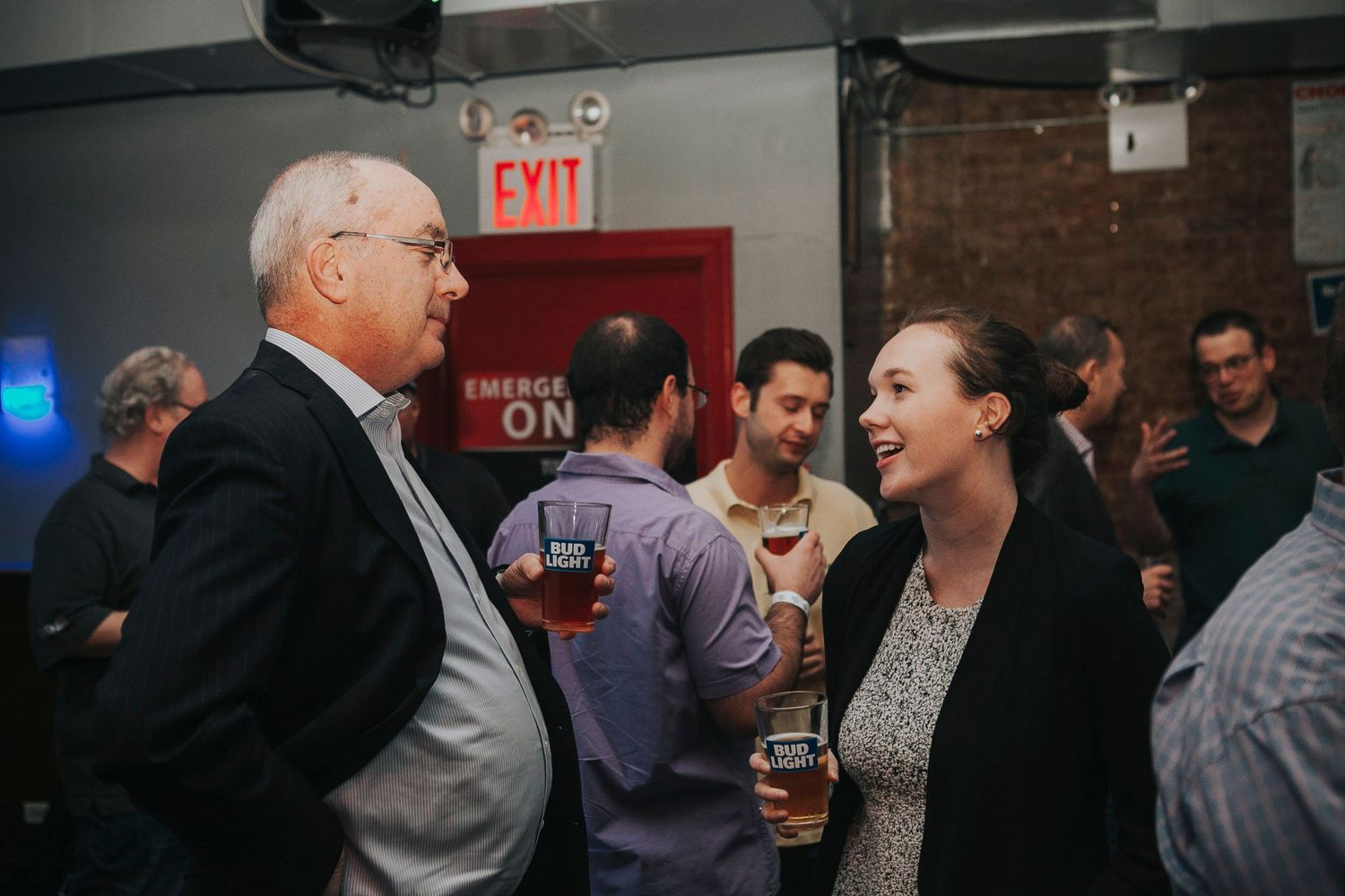 Man and woman engage in conversation at a dimly lit bar event.