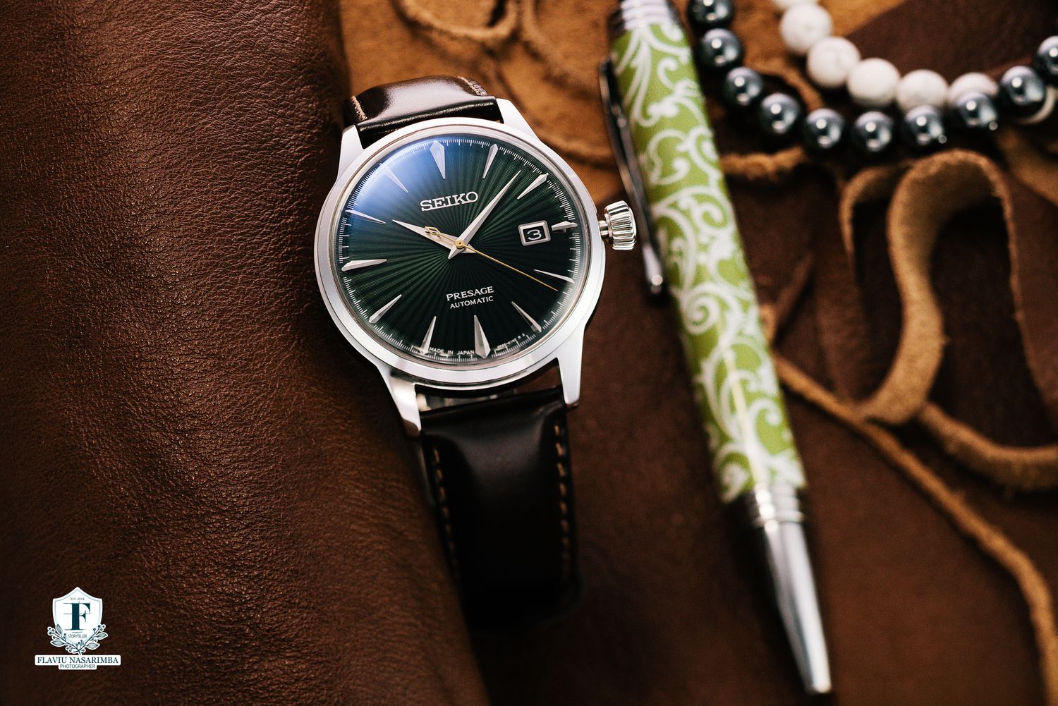 Seiko Presage automatic watch with green dial on brown leather strap beside a decorative pen and beads.