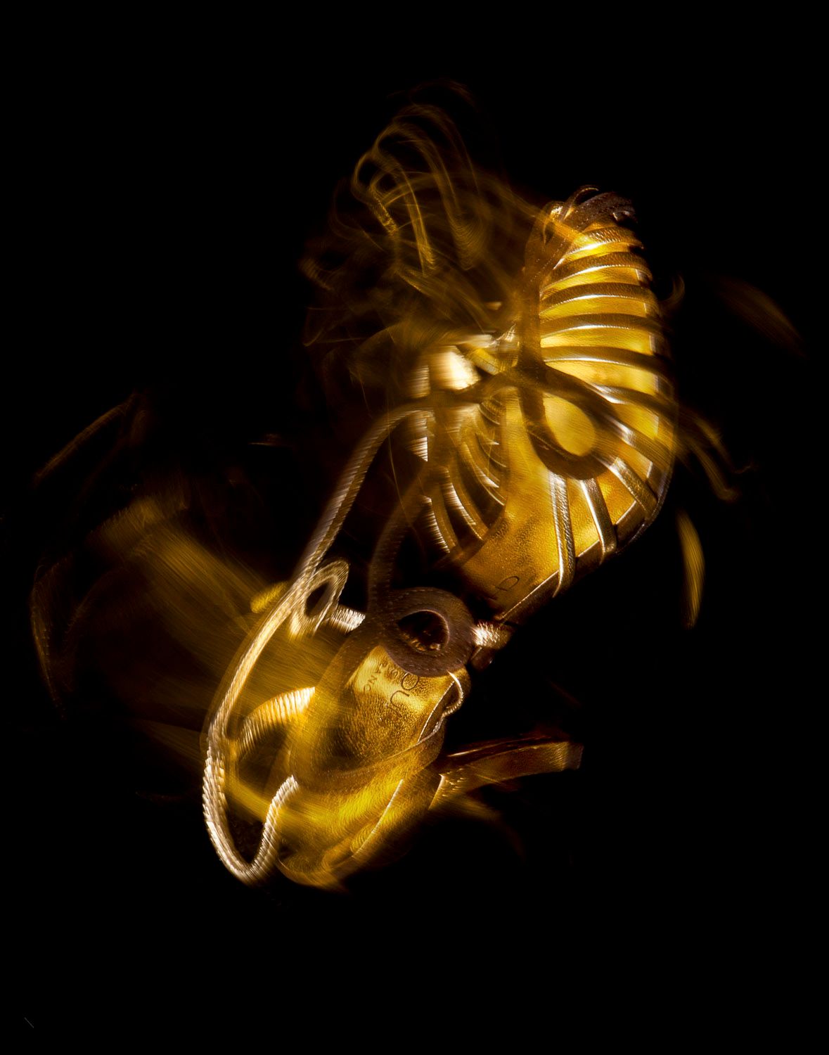 Abstract long exposure photograph of golden jewelry pieces creating a blurred motion effect on black background.