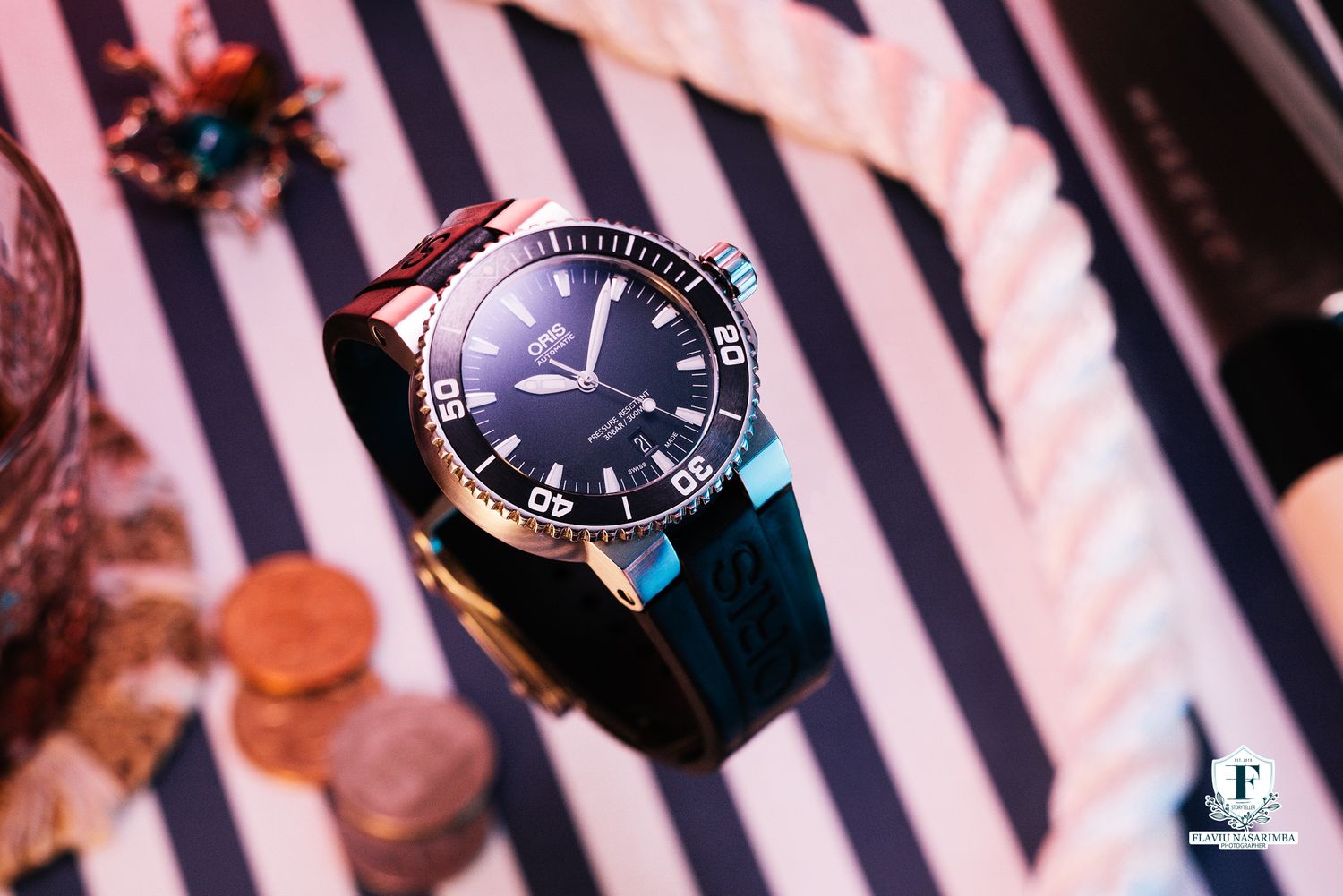 Oris Aquis diver watch with black bezel and rubber strap on nautical striped background.