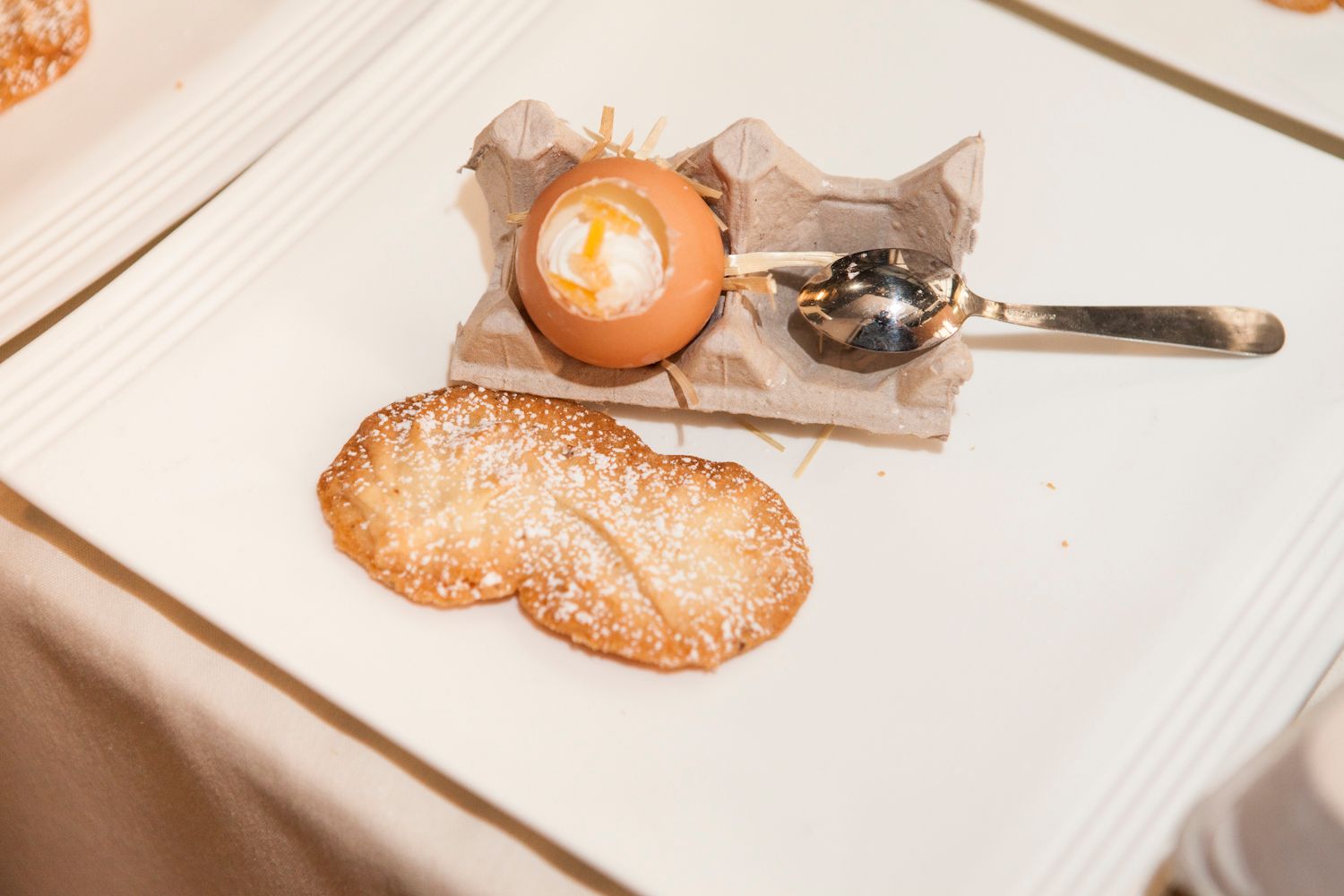 Elegant soft-boiled egg served in shell with crispy sugar-dusted tuile cookies on a white tablecloth.