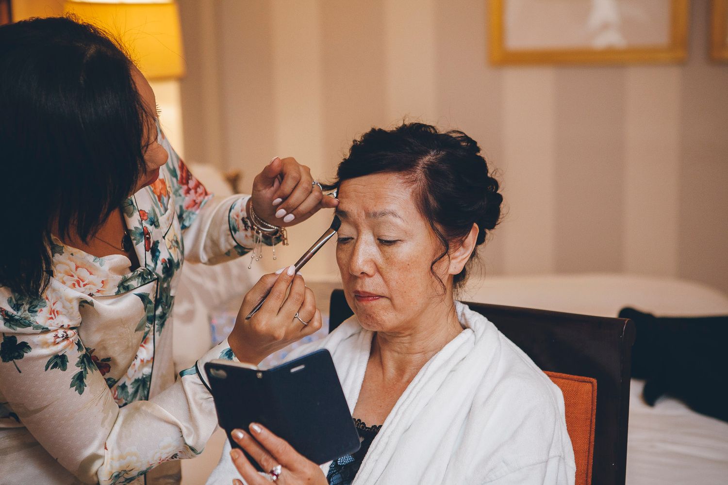 Asian woman getting professional makeup applied by makeup artist before wedding ceremony.