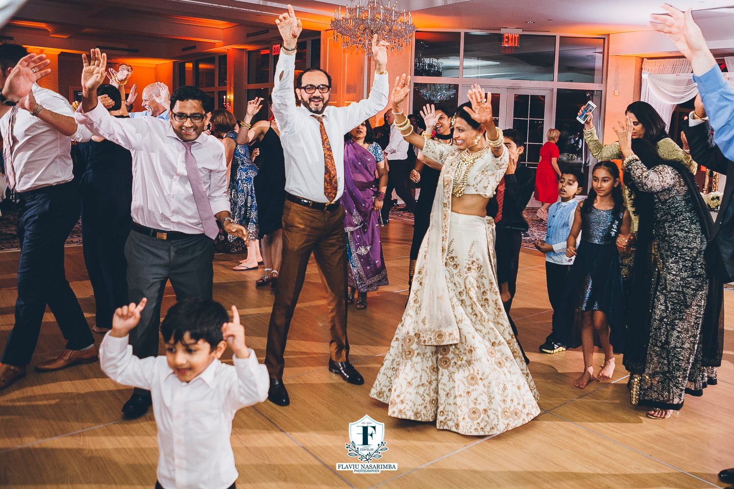 Lively Indian wedding reception dance floor filled with celebrating guests in elegant gold-lit ballroom.