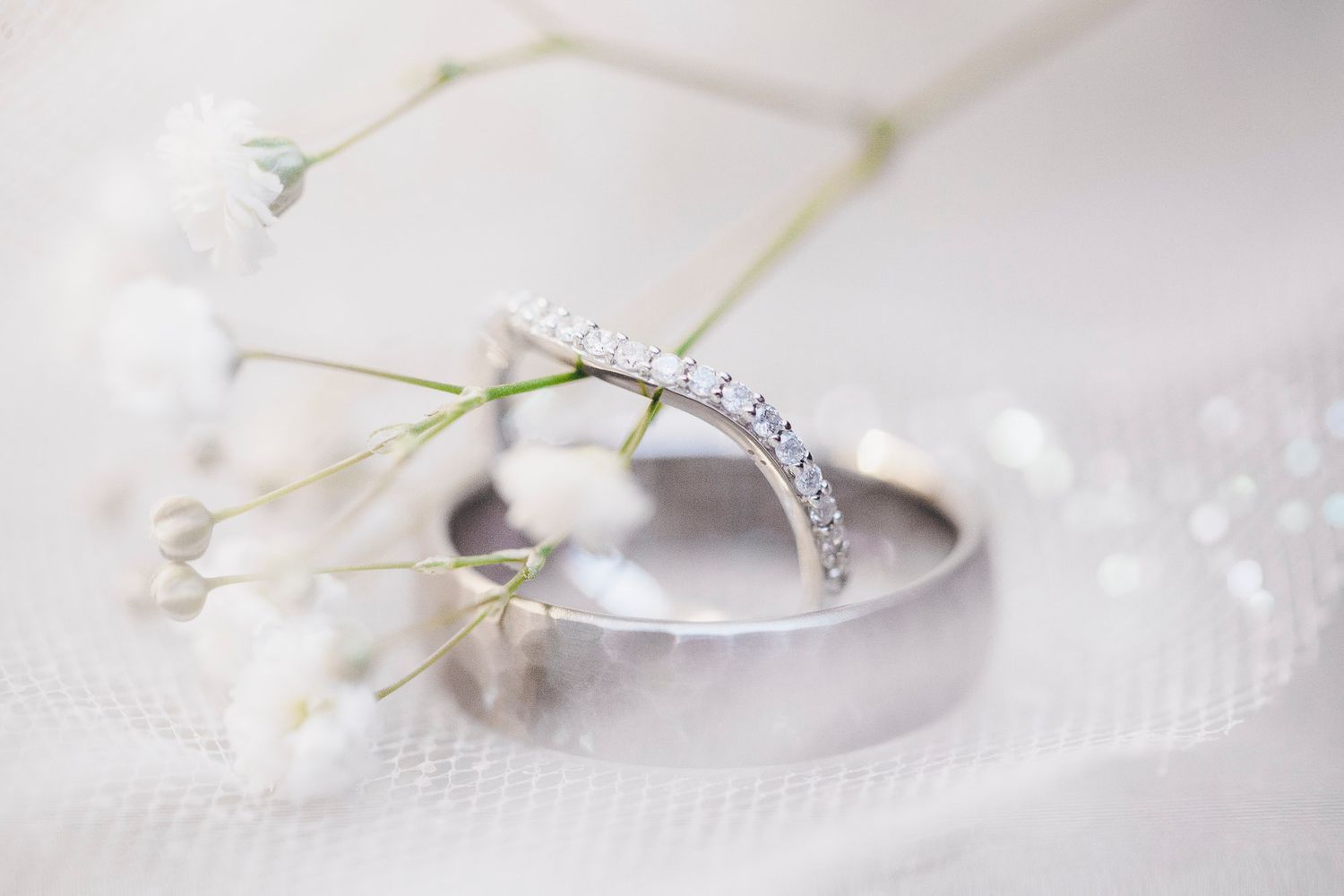 Close-up of diamond wedding band and plain gold ring resting on white fabric with delicate baby's breath flowers.