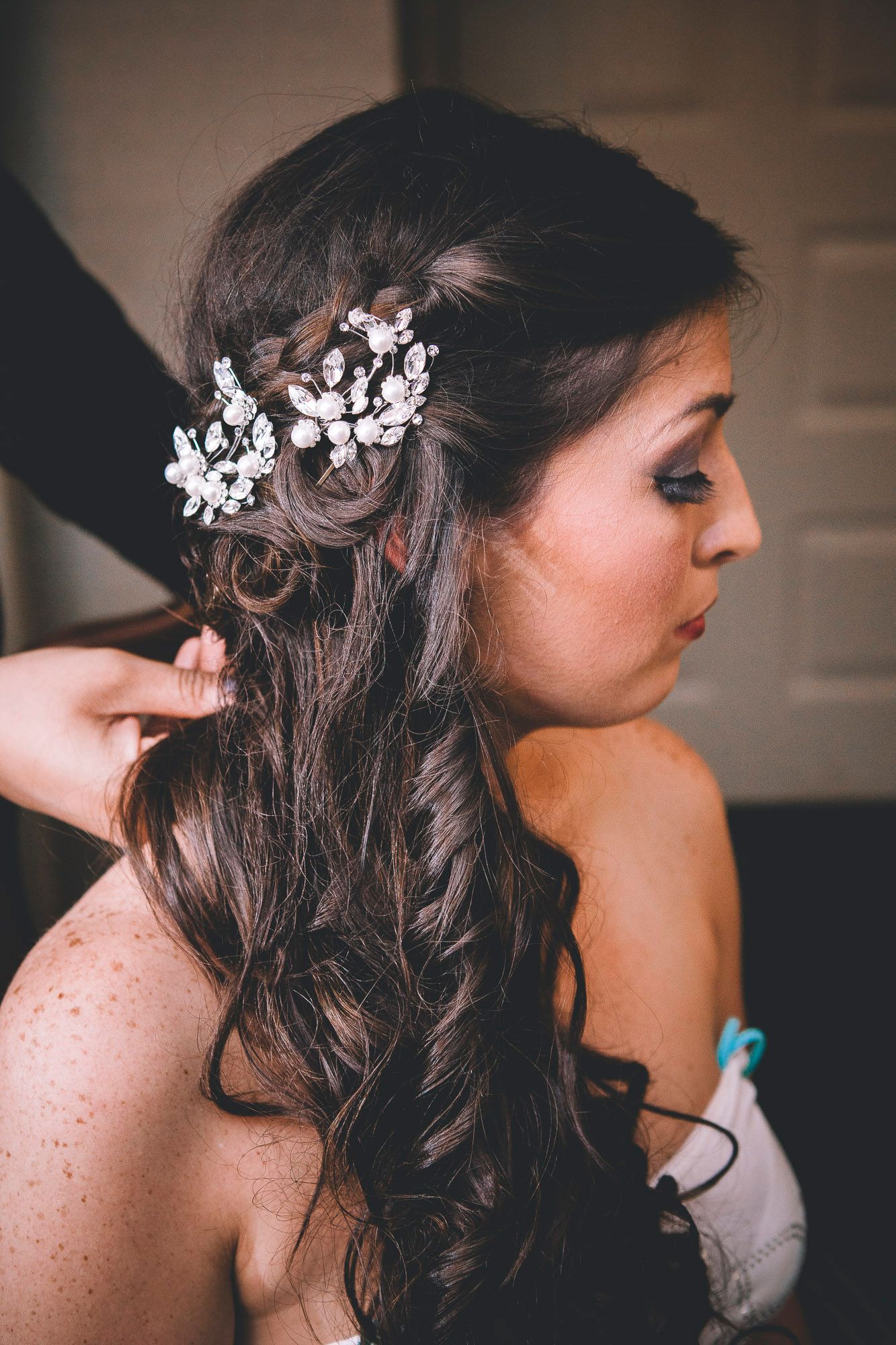 Bride with long curly brown hair having a floral crystal hair accessory placed by a stylist before wedding.