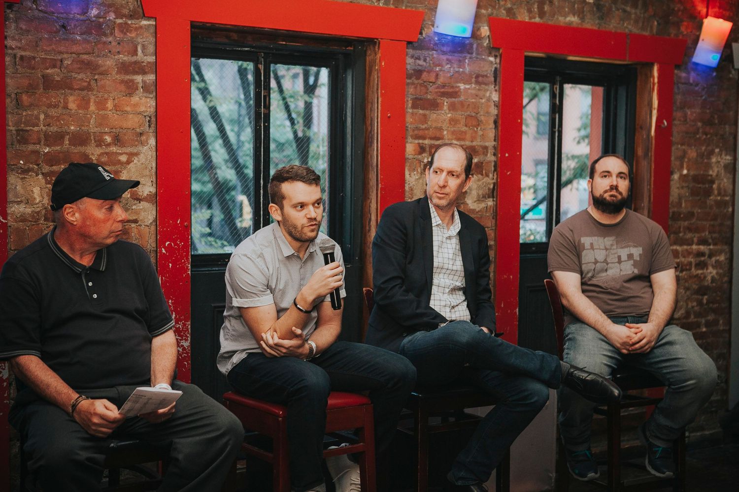 Four men seated at a panel discussion in a brick-walled bar venue.