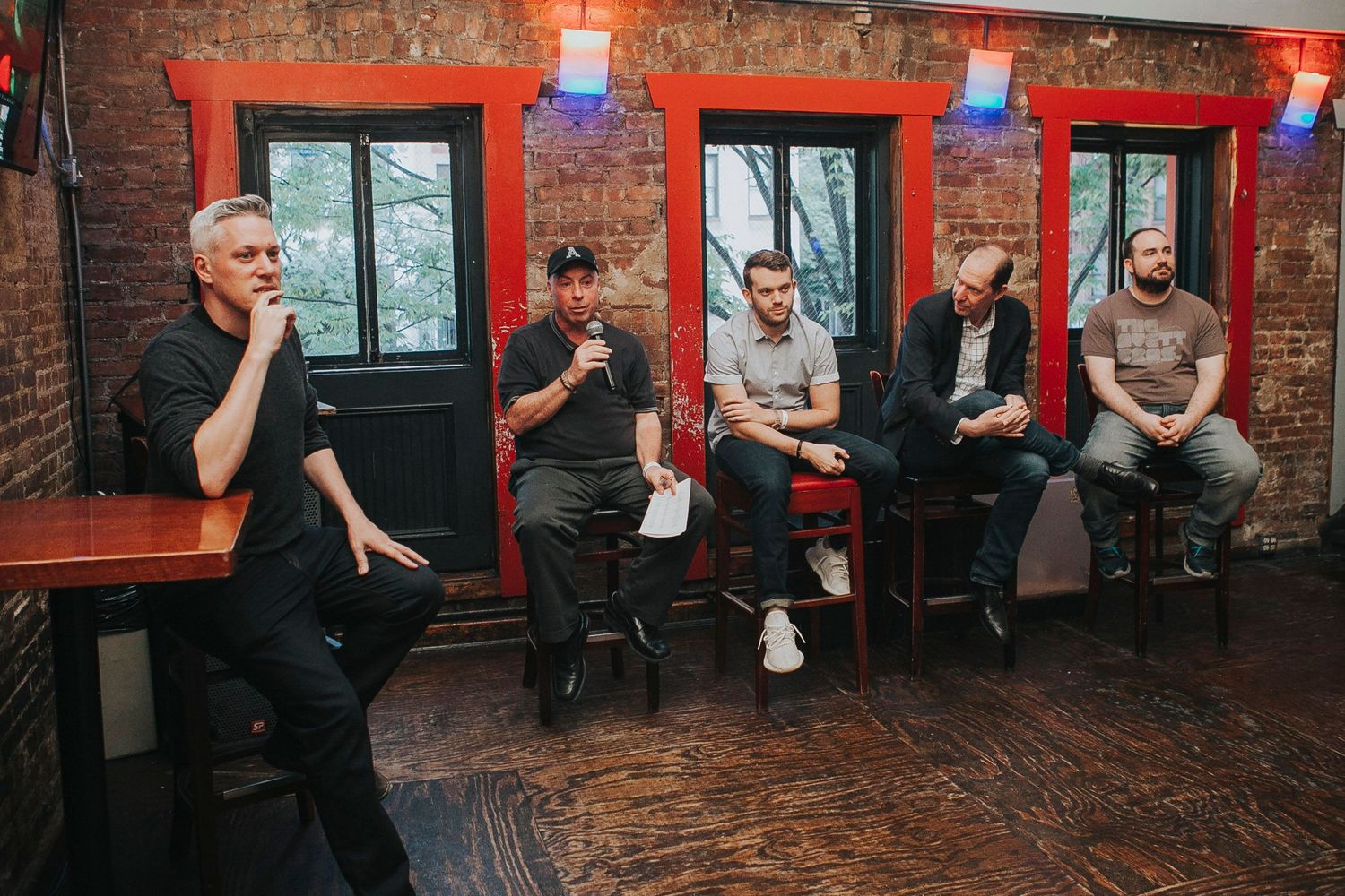 Five men seated on stools in a rustic brick bar venue during a panel discussion event.