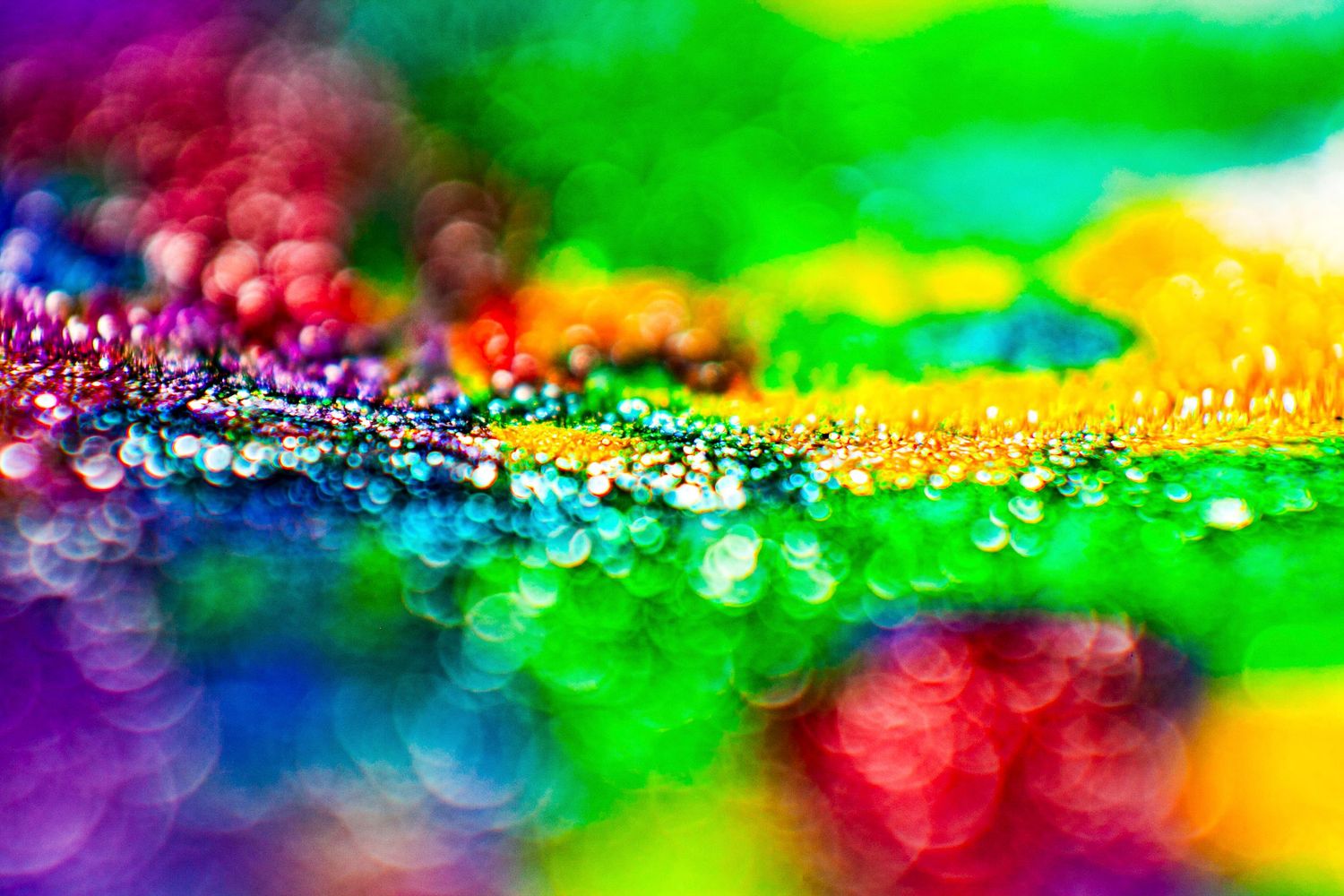 Vibrant macro photo of colorful bokeh lights with sparkling water droplets in rainbow hues of green, purple, blue, and orange.