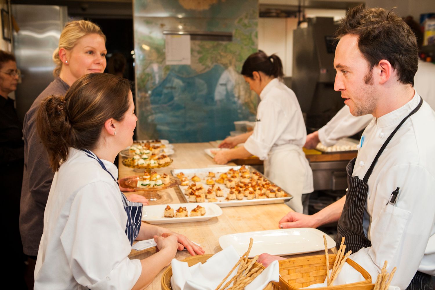 Catering staff in white chef uniforms preparing and plating appetizers in a restaurant kitchen.