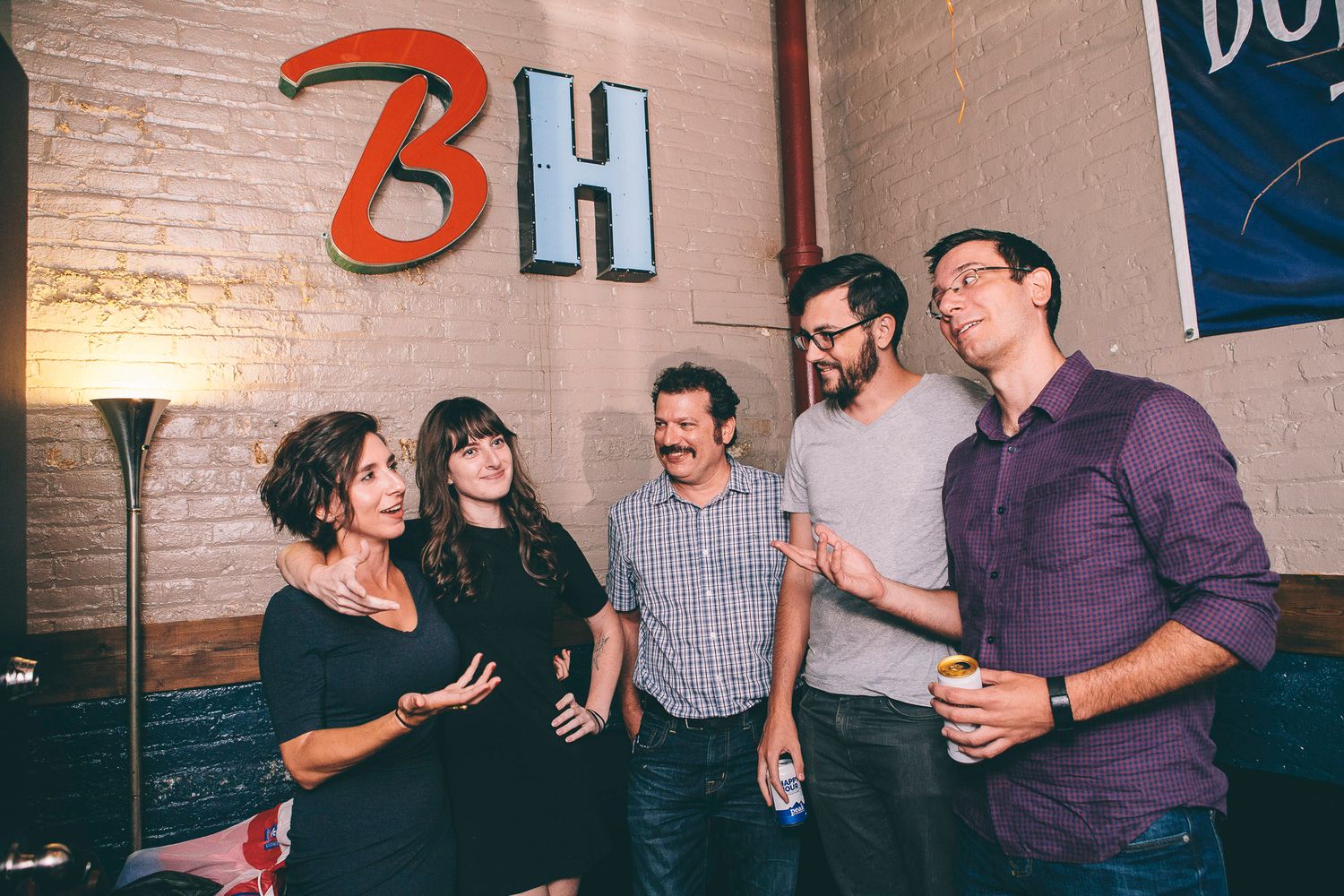 Group of five people laughing and chatting at a casual social event in a trendy bar.