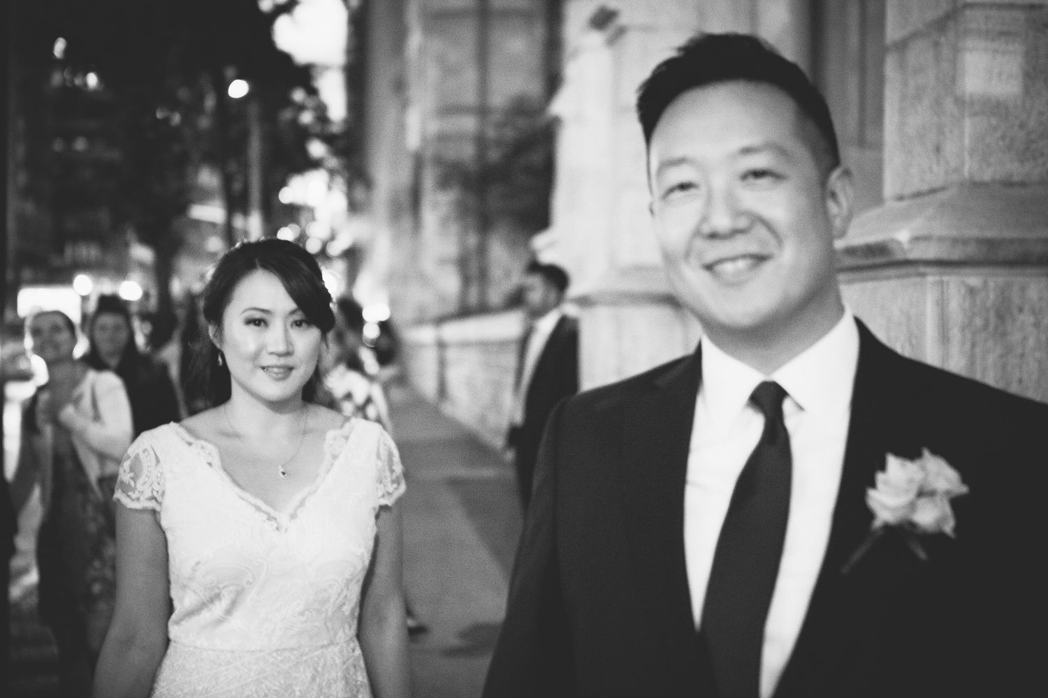 Bride and groom smile together on a busy city street in classic black and white photo.