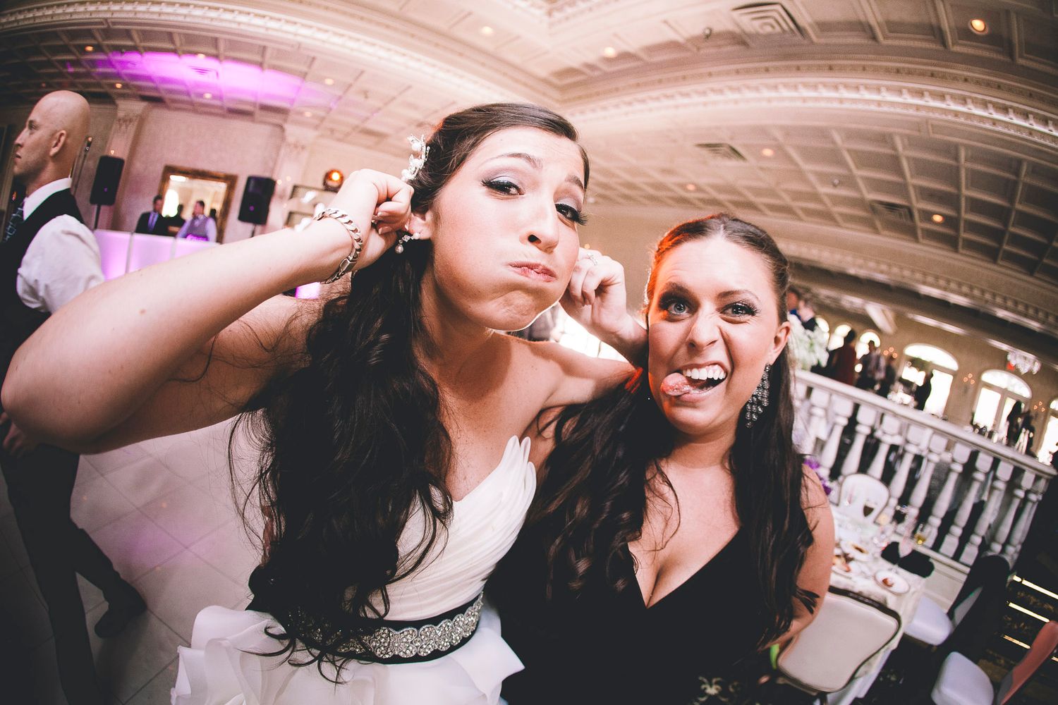 Bride and friend make playful faces for a fun fisheye lens photo at wedding reception.