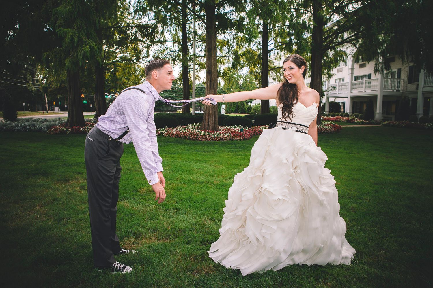 Bride and groom hold hands playfully on green lawn during outdoor wedding photo session.
