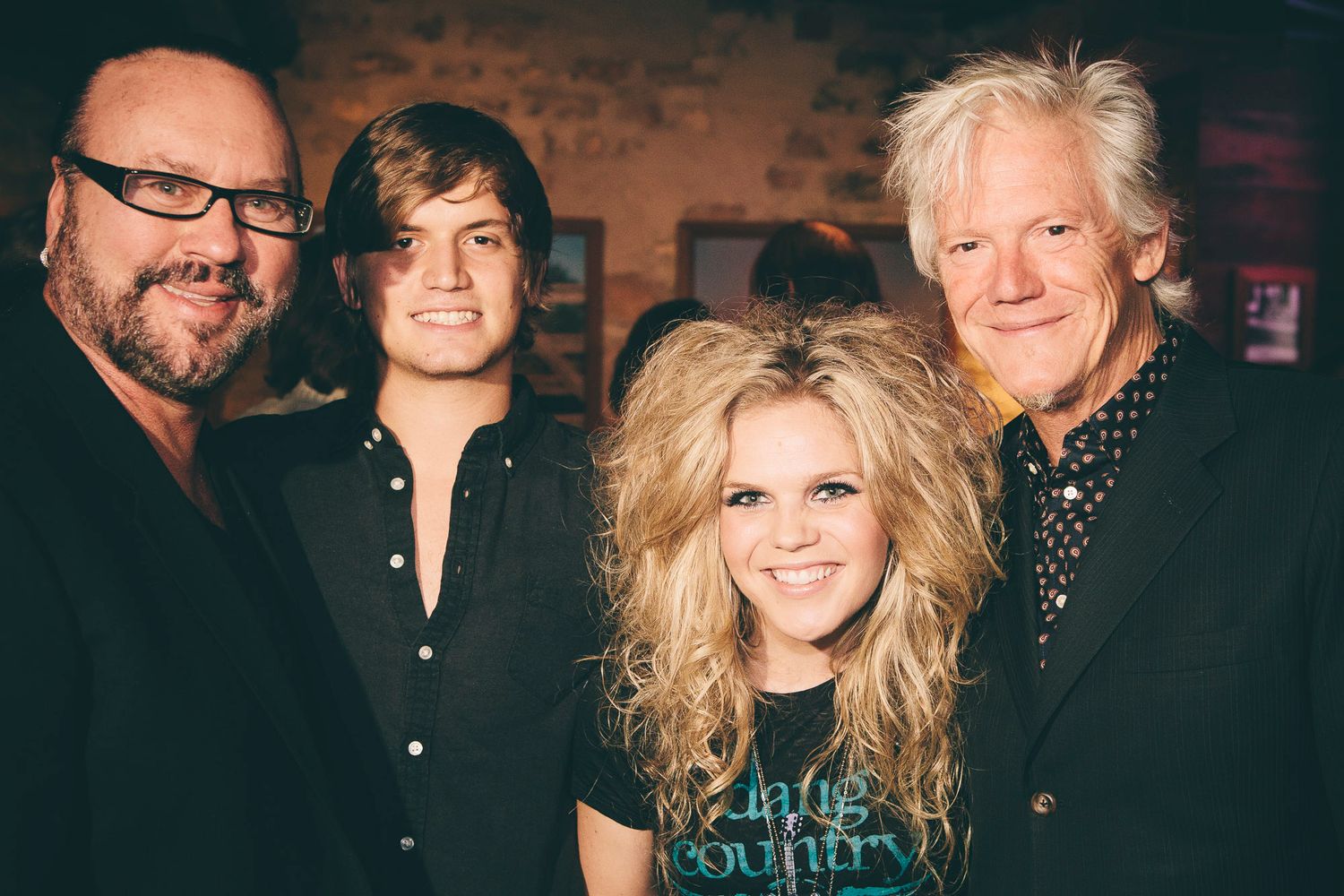 Four people pose together smiling at a country music event in a rustic venue.