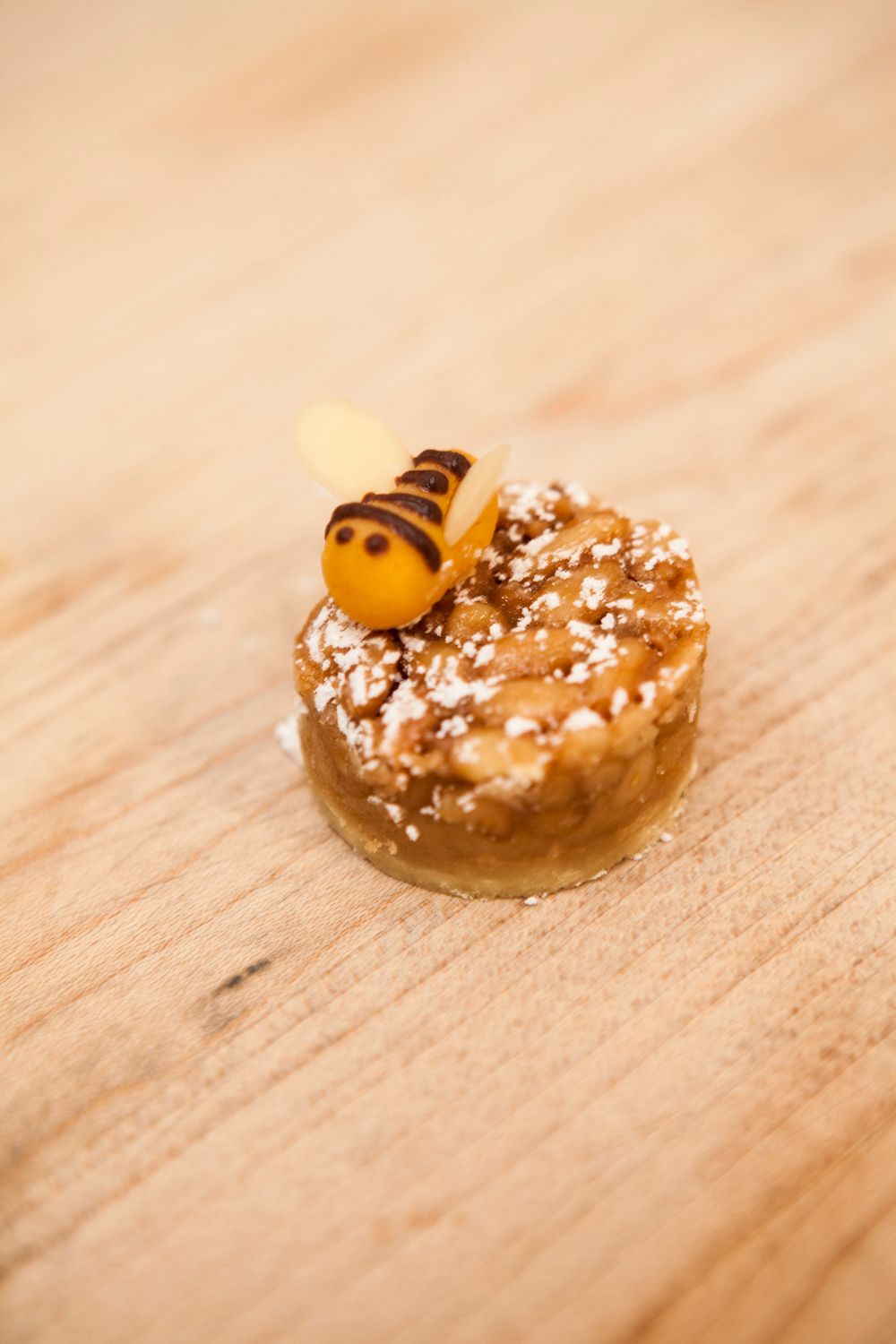 Delicate caramel pastry tart topped with a decorative sugar bee on a wooden surface.