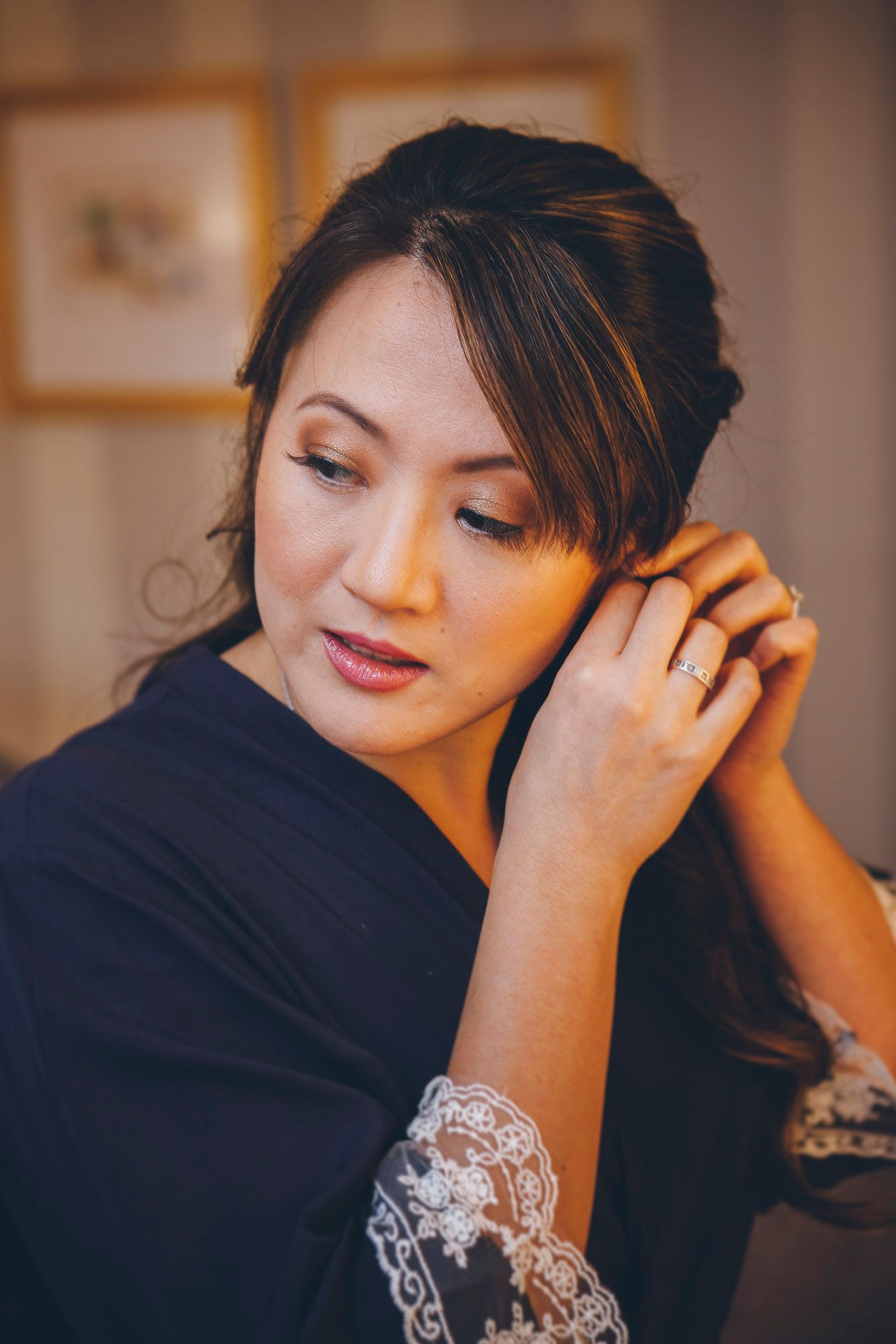 Asian bride adjusting her earring while wearing a navy lace robe during wedding preparations.