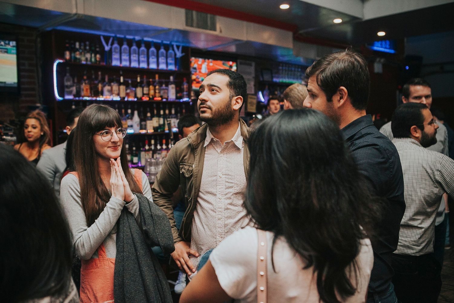 Group of young adults socializing and conversing in front of a well-stocked bar.