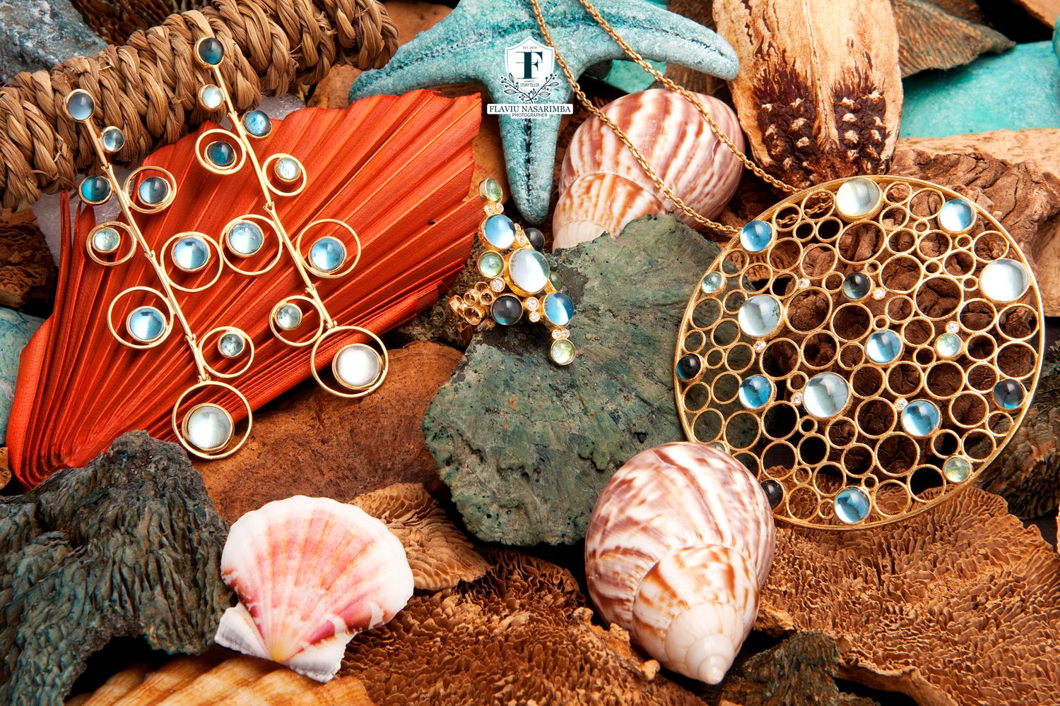 Gold jewelry set with blue gemstones displayed on seashells and coastal natural elements.