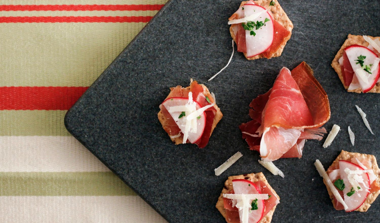 Elegant prosciutto and cream cheese appetizer bites served on a dark slate board with herb garnish.
