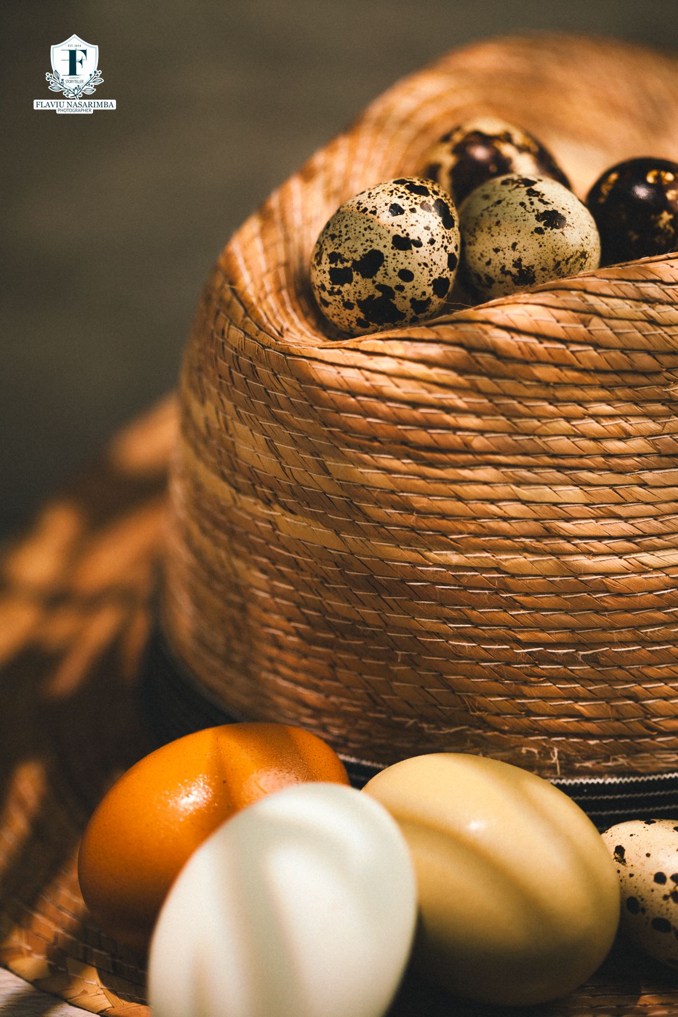 Speckled quail eggs arranged on a woven basket surrounded by colorful Easter eggs on wood.