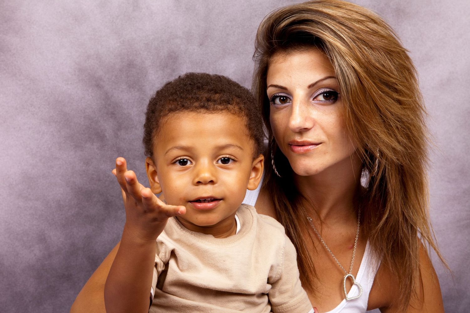 Young mother with long blonde hair holding smiling toddler boy in studio portrait.