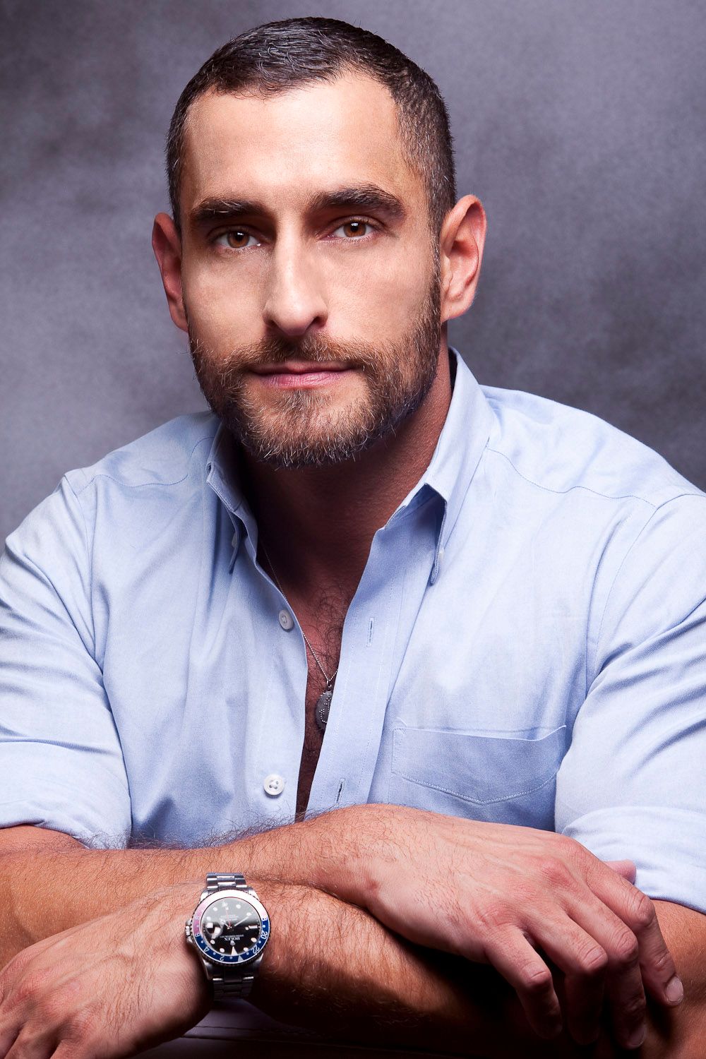 Bearded man in blue shirt with watch posing for a casual professional portrait photo.