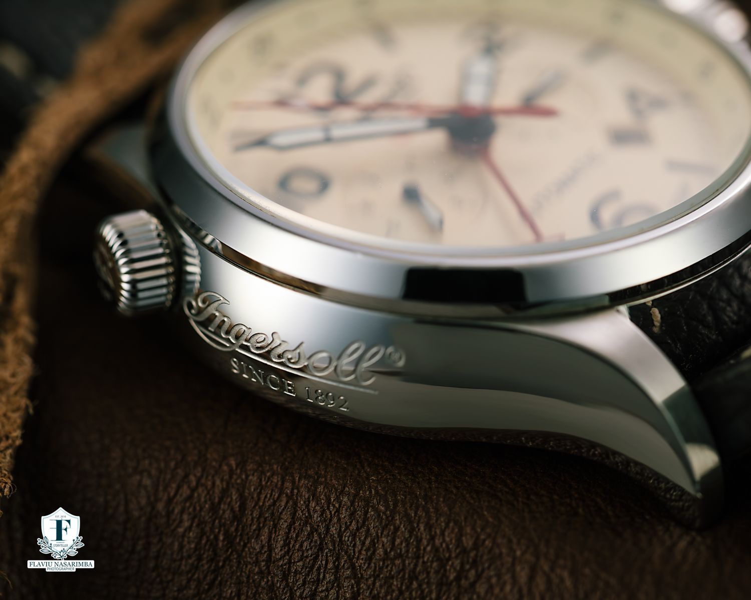 Close-up of an Ingersoll stainless steel watch case showing engraved branding and crown detail on leather.