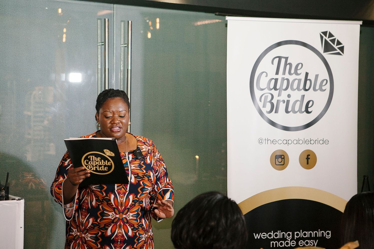 Speaker presenting at The Capable Bride wedding planning event at a podium with branded signage.