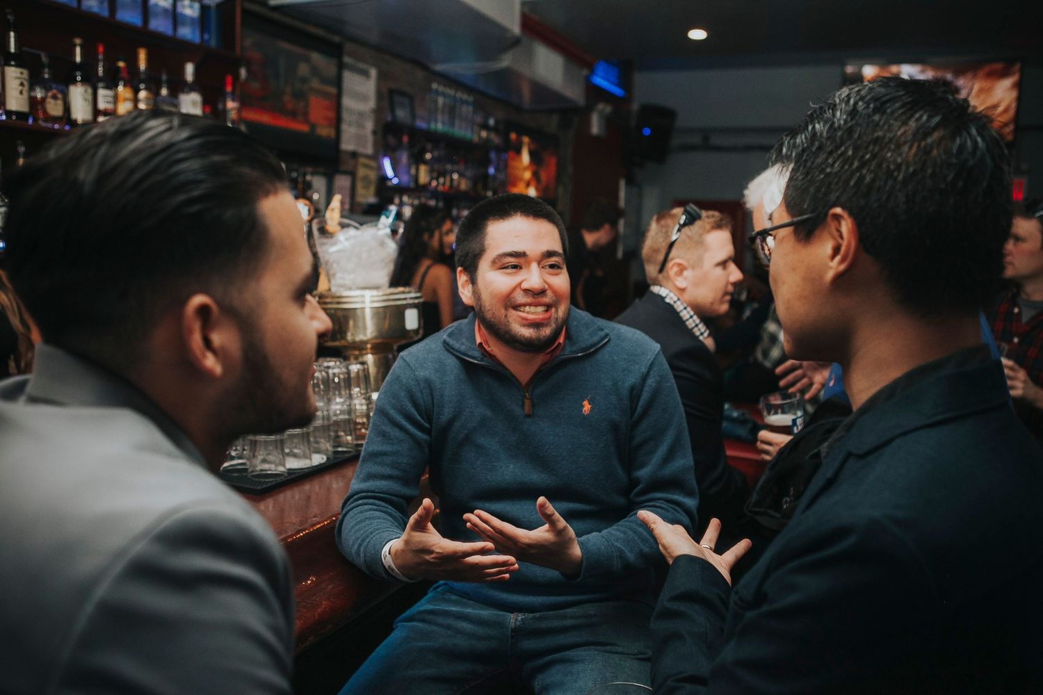 Three men engage in lively conversation at a bar during a social networking event.