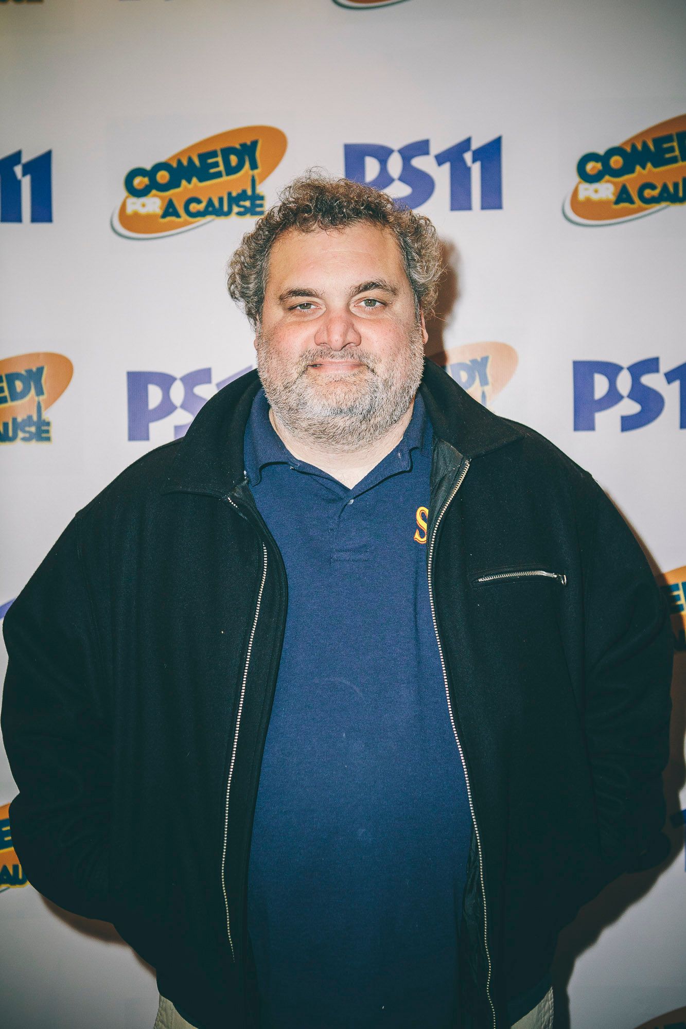 Man in black jacket and blue shirt posing at PS11 Comedy for a Cause event.