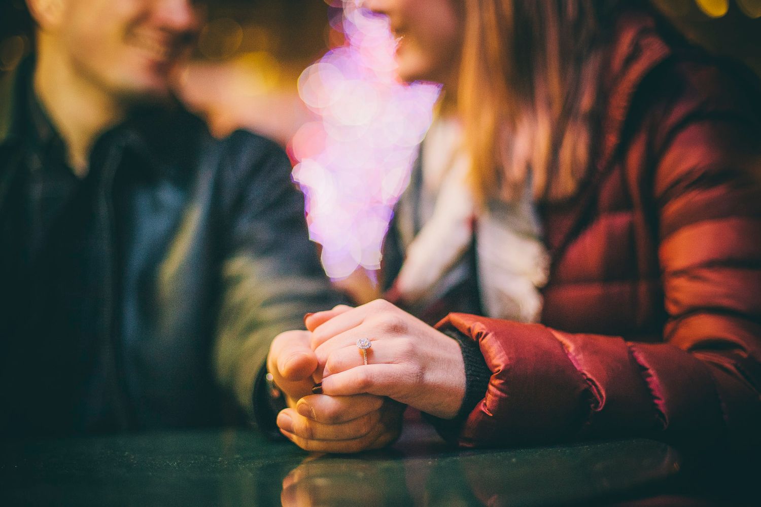 Couple holding hands with purple smoke heart bokeh at romantic night date.