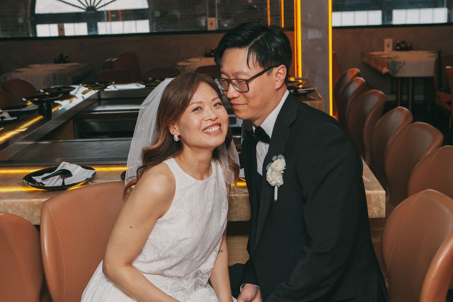 Happy Asian bride laughs as groom whispers in her ear at wedding reception venue.