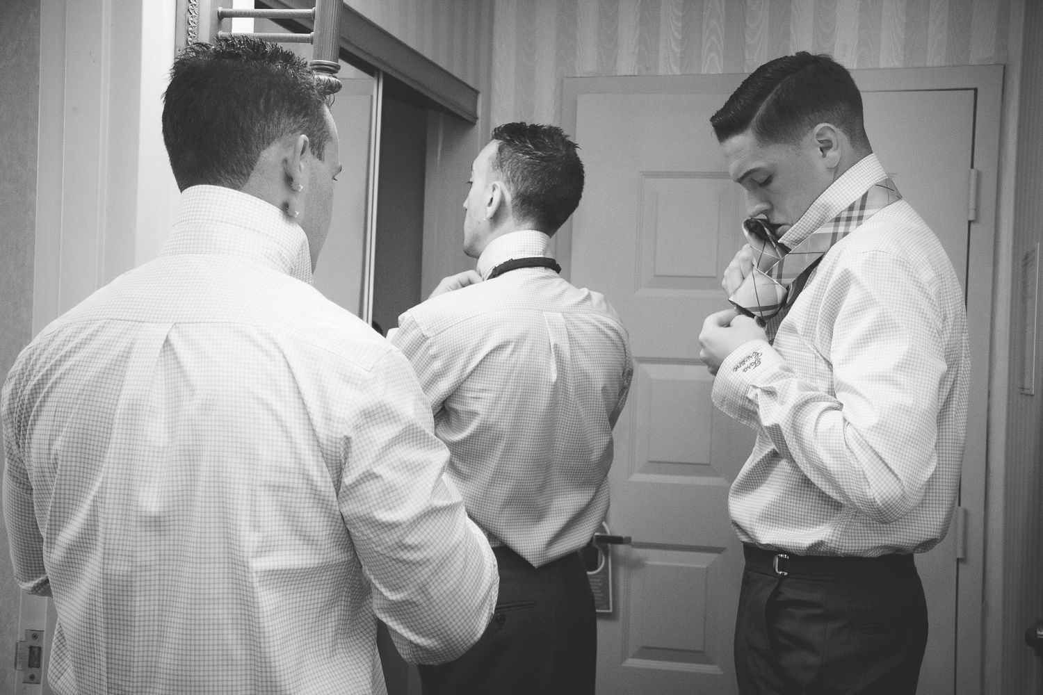 Black and white photo of groomsmen helping each other adjust bowties while getting ready for wedding.